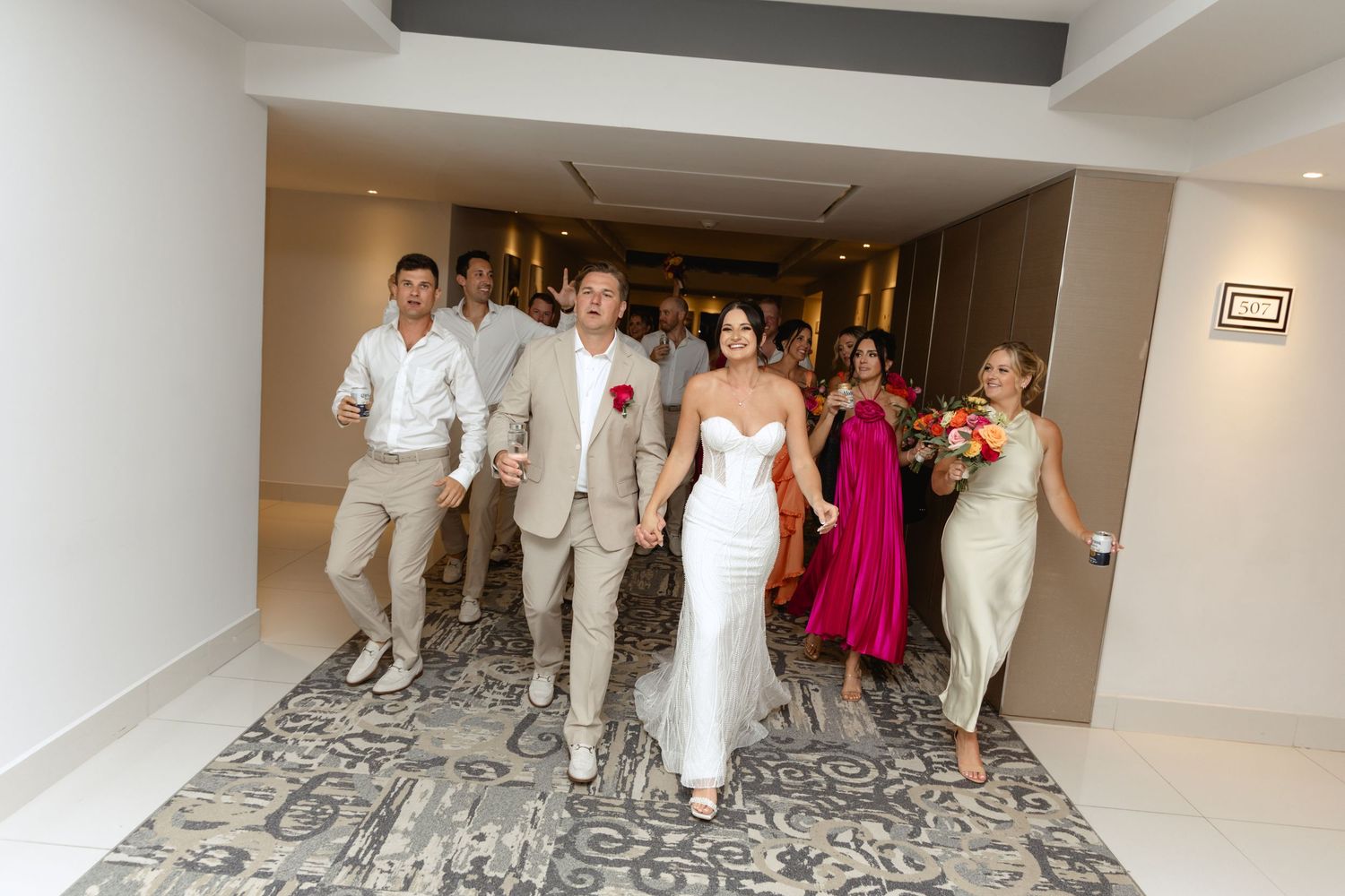Wedding party walking through hotel hallway with patterned carpet.