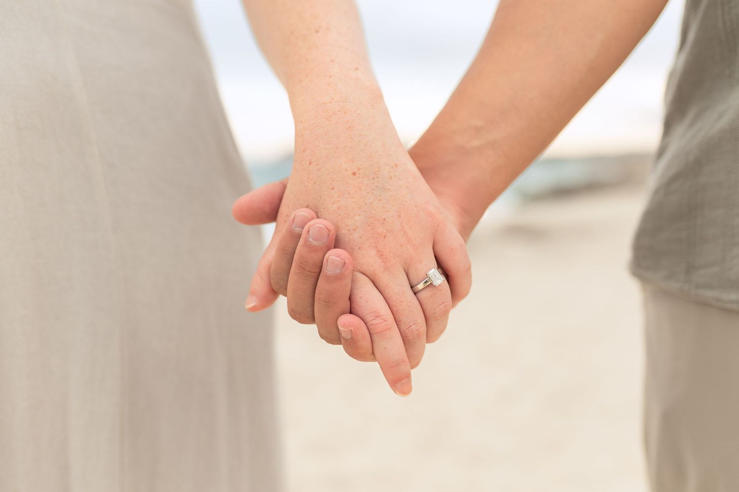 Close-up view of two people holding hands with an engagement ring visible.