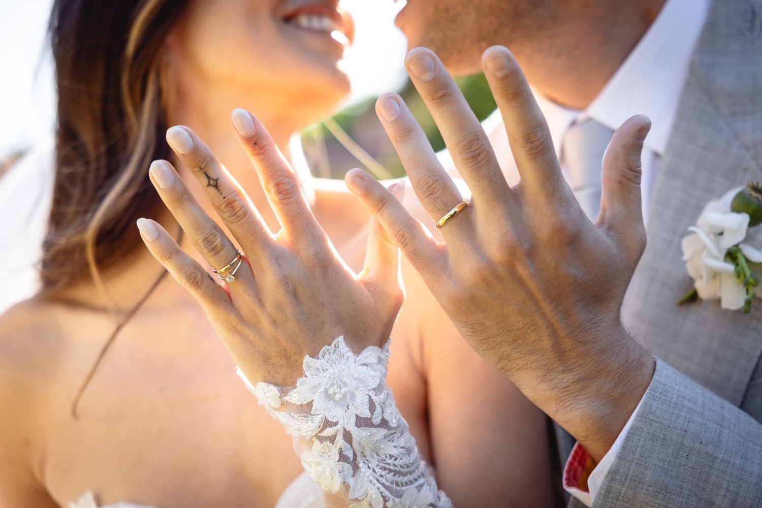 Close-up of hands showing wedding rings in sunlight with lace detail visible.