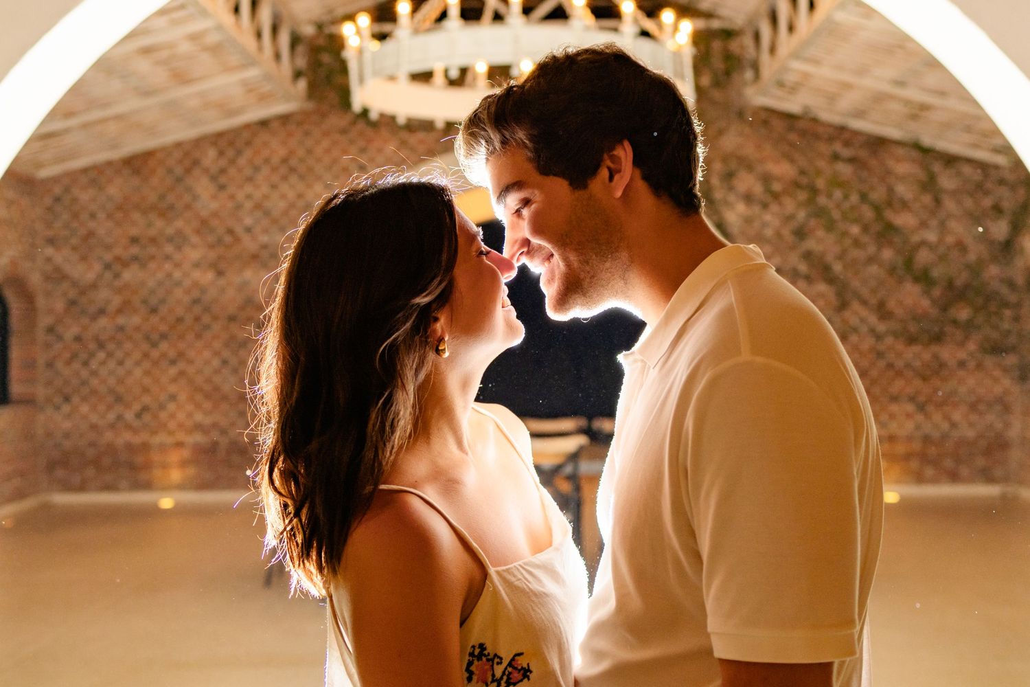 A couple shares an intimate dance together in a rustic indoor venue with exposed brick walls.