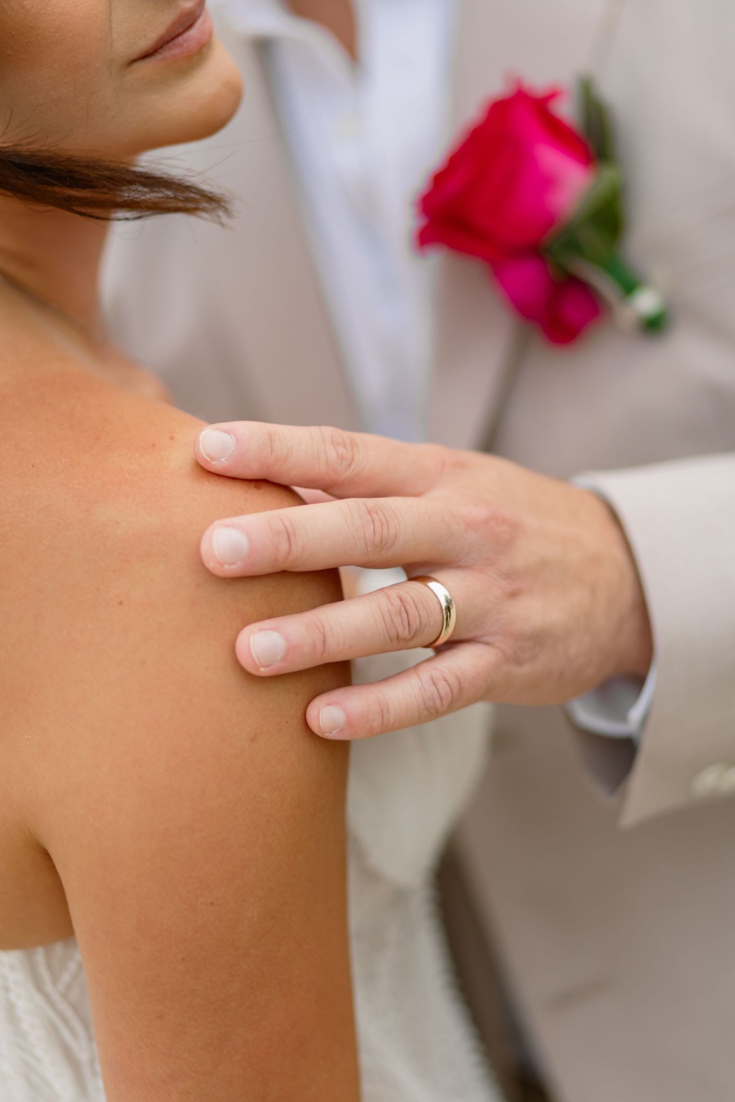 Close-up details of hands and rings during a beach wedding ceremony.