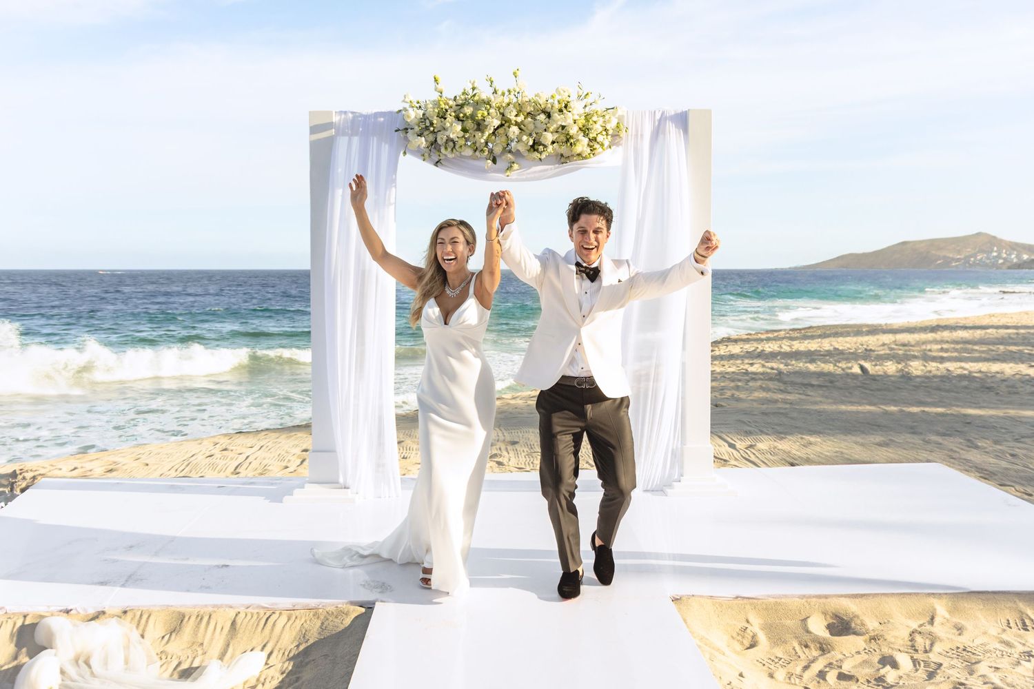 Beach wedding ceremony site with white floral arch and ocean backdrop.
