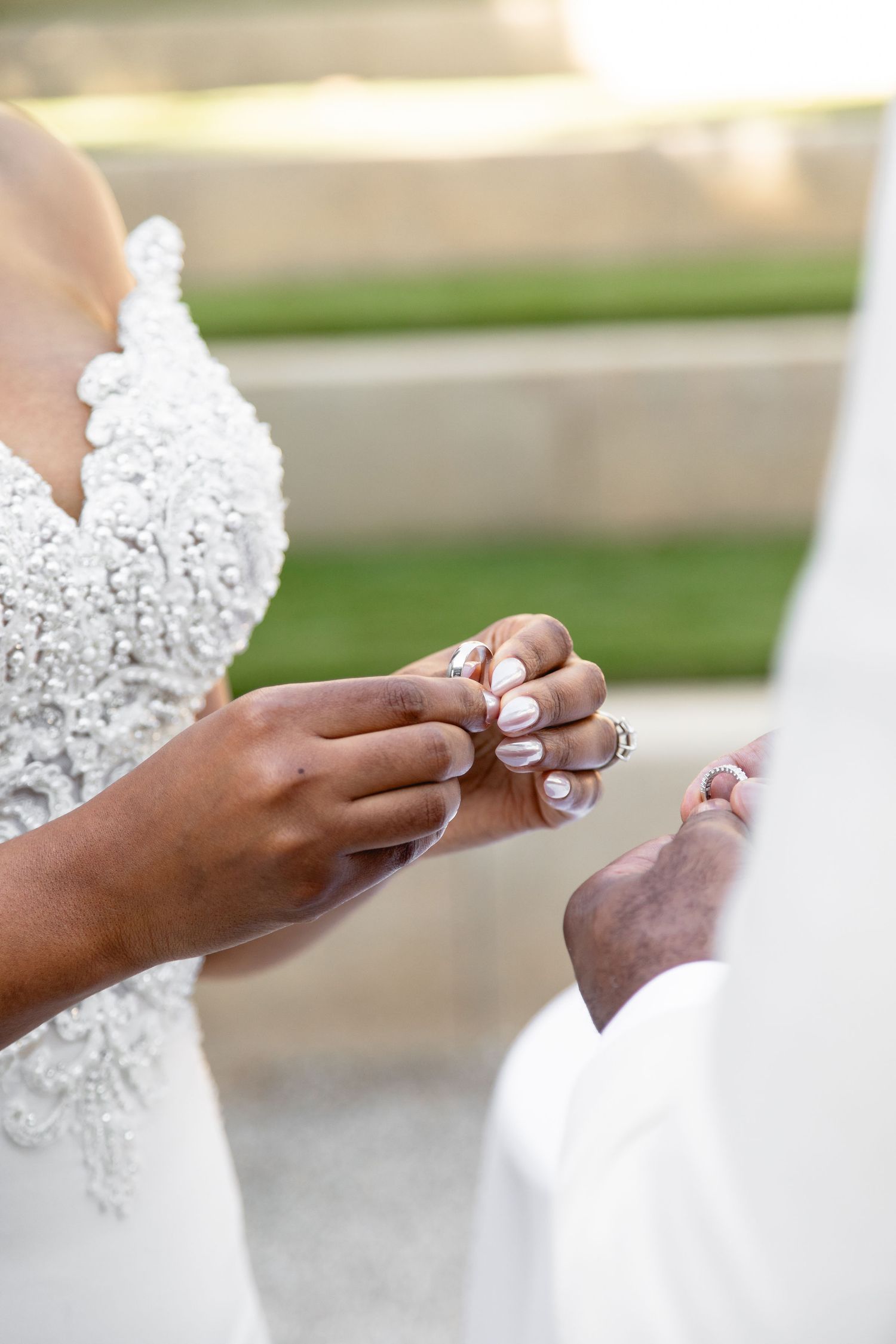 Close-up of hands exchanging rings during wedding ceremony, showing detailed lace wedding dress bodice.