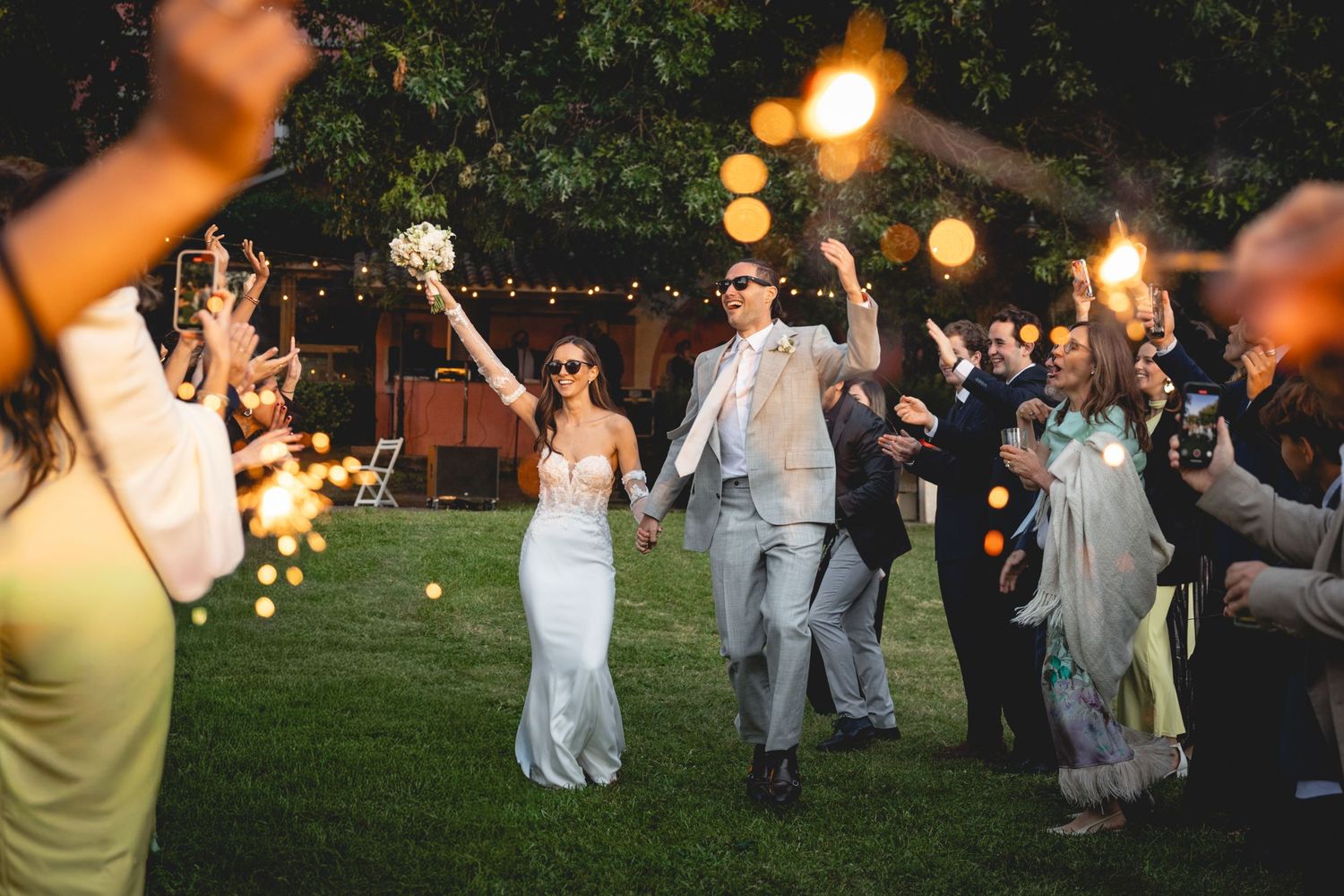 Wedding reception guests dancing outdoors under string lights at dusk.