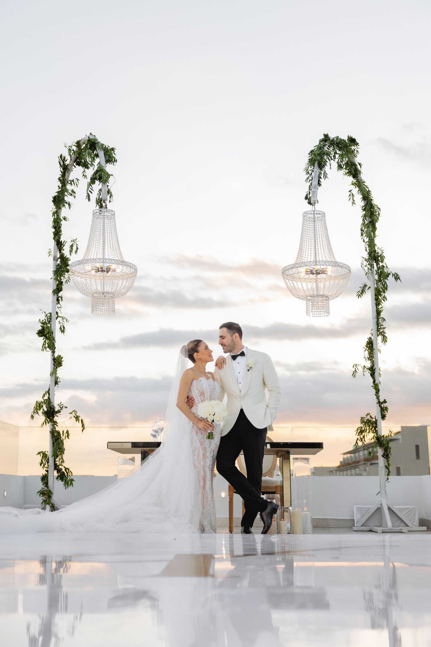 Romantic rooftop wedding scene with hanging chandeliers and vine decorations at sunset.