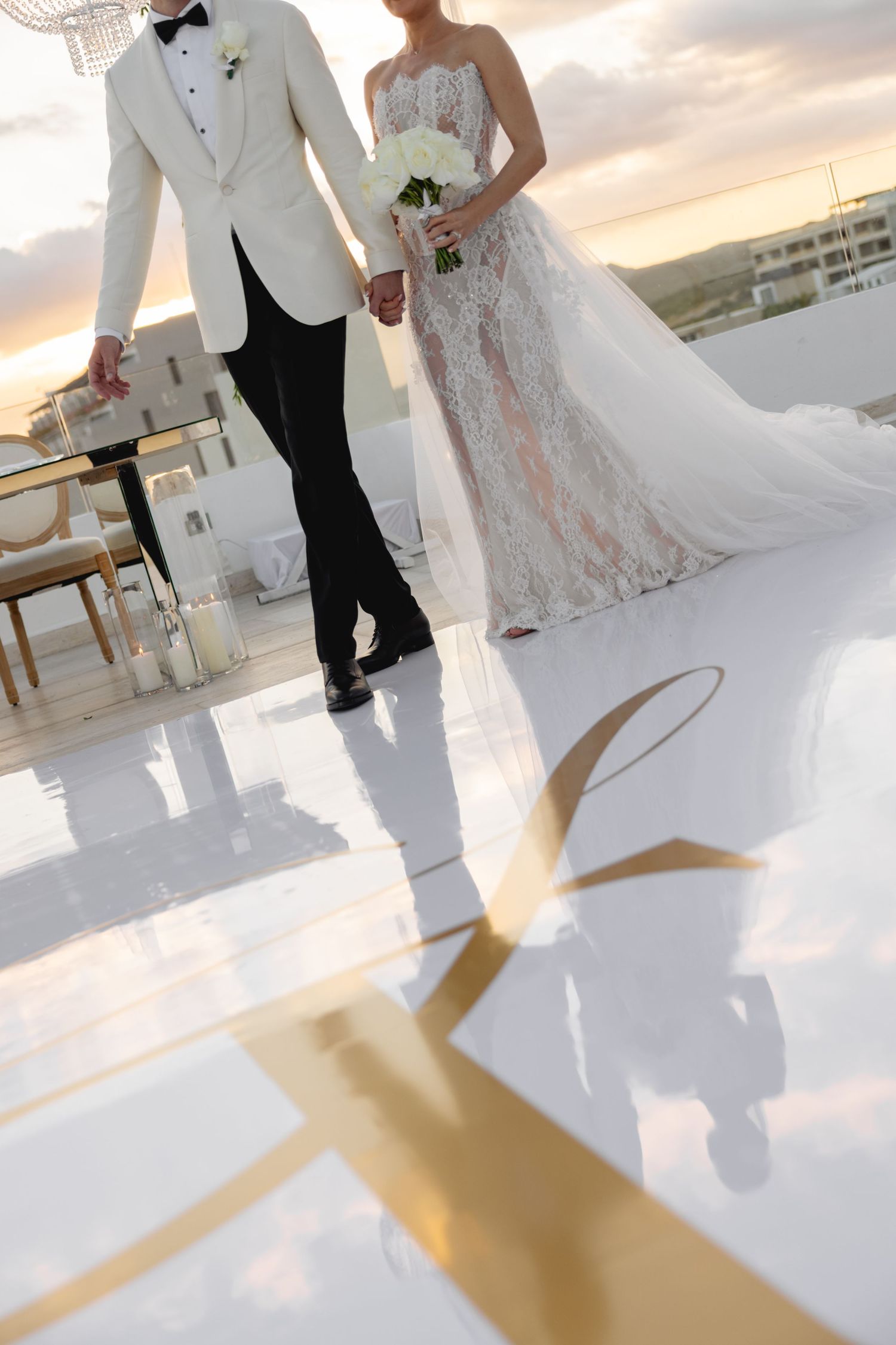Wedding couple's feet and dress hem dancing on a reflective white floor during sunset.