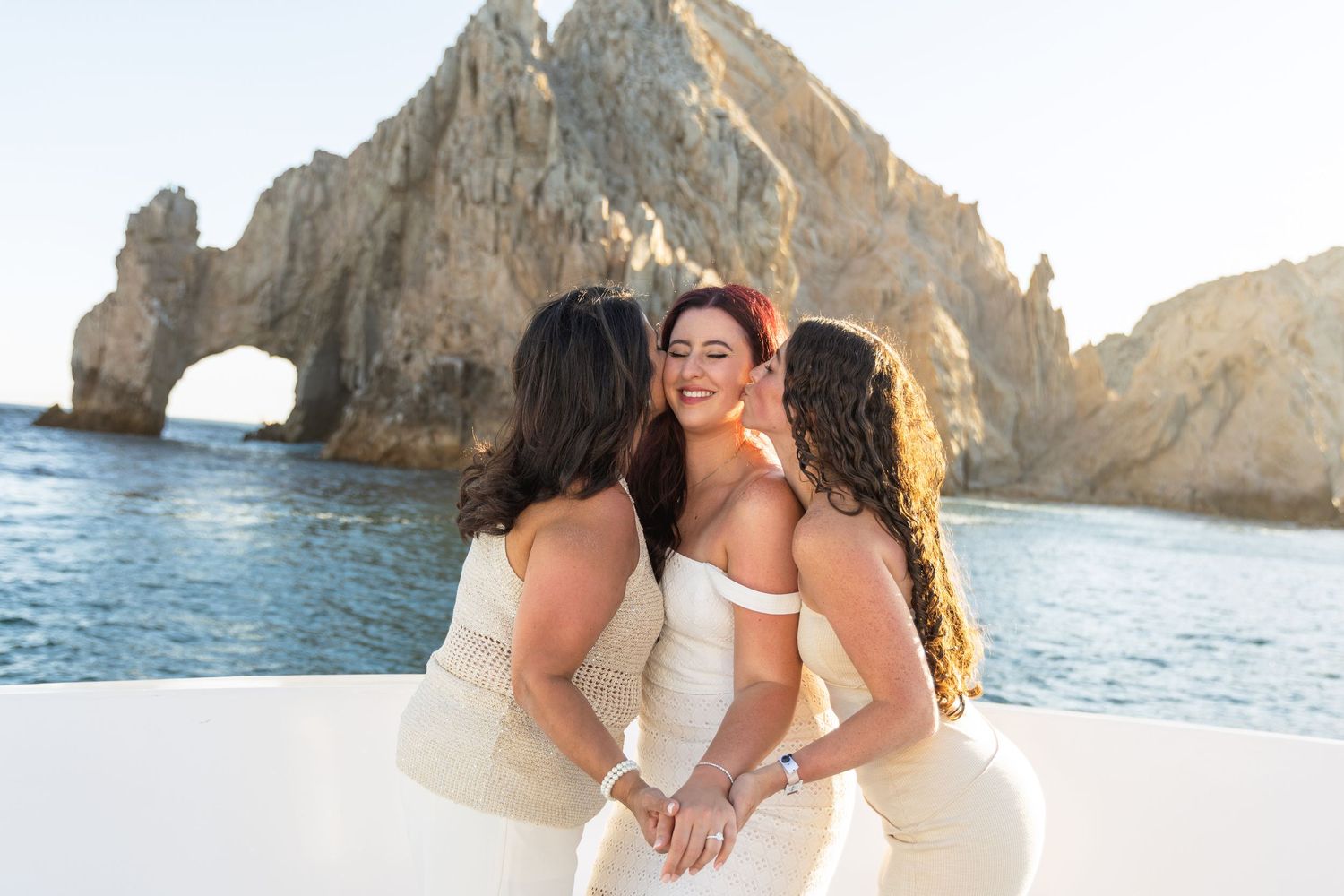 Romantic couple embracing on sandy beach near rocky cliffs at sunset in Cabo San Lucas, Mexico.
