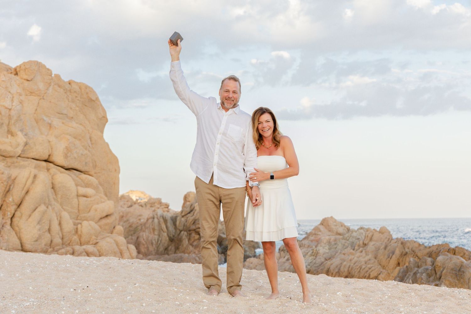 A couple in white wedding attire poses together on scenic desert rock formations at sunset.