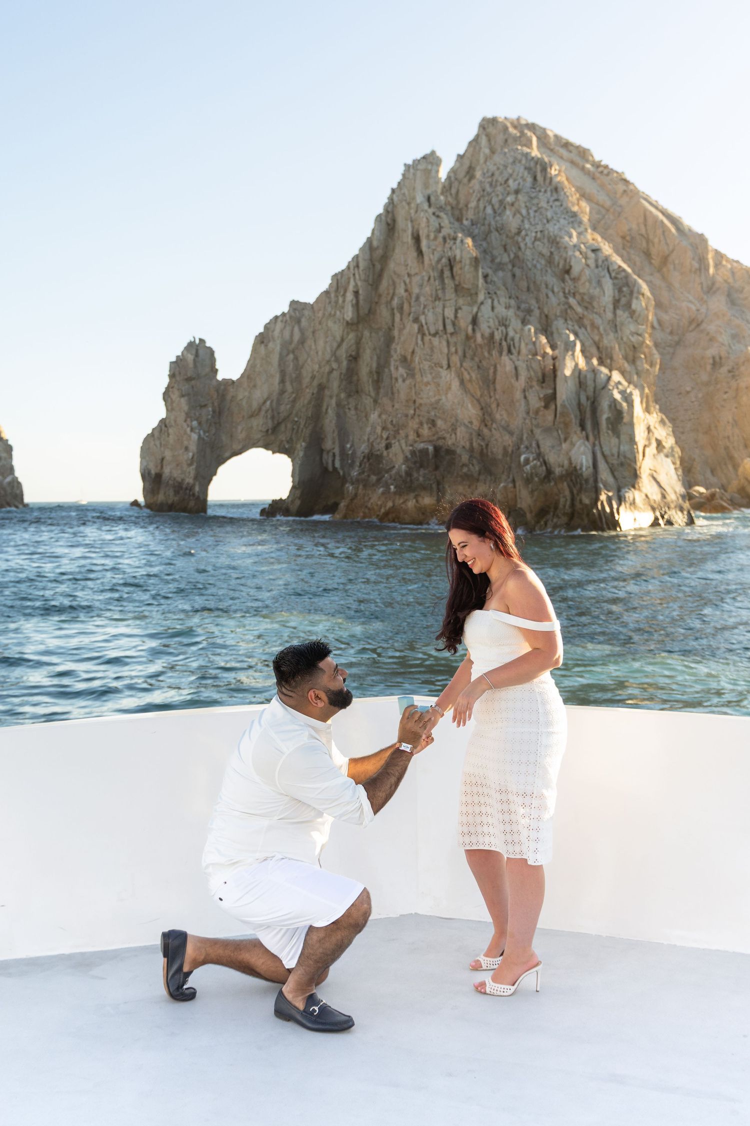 A romantic proposal moment unfolds on a boat with the iconic Los Cabos Arch rock formation in the background.