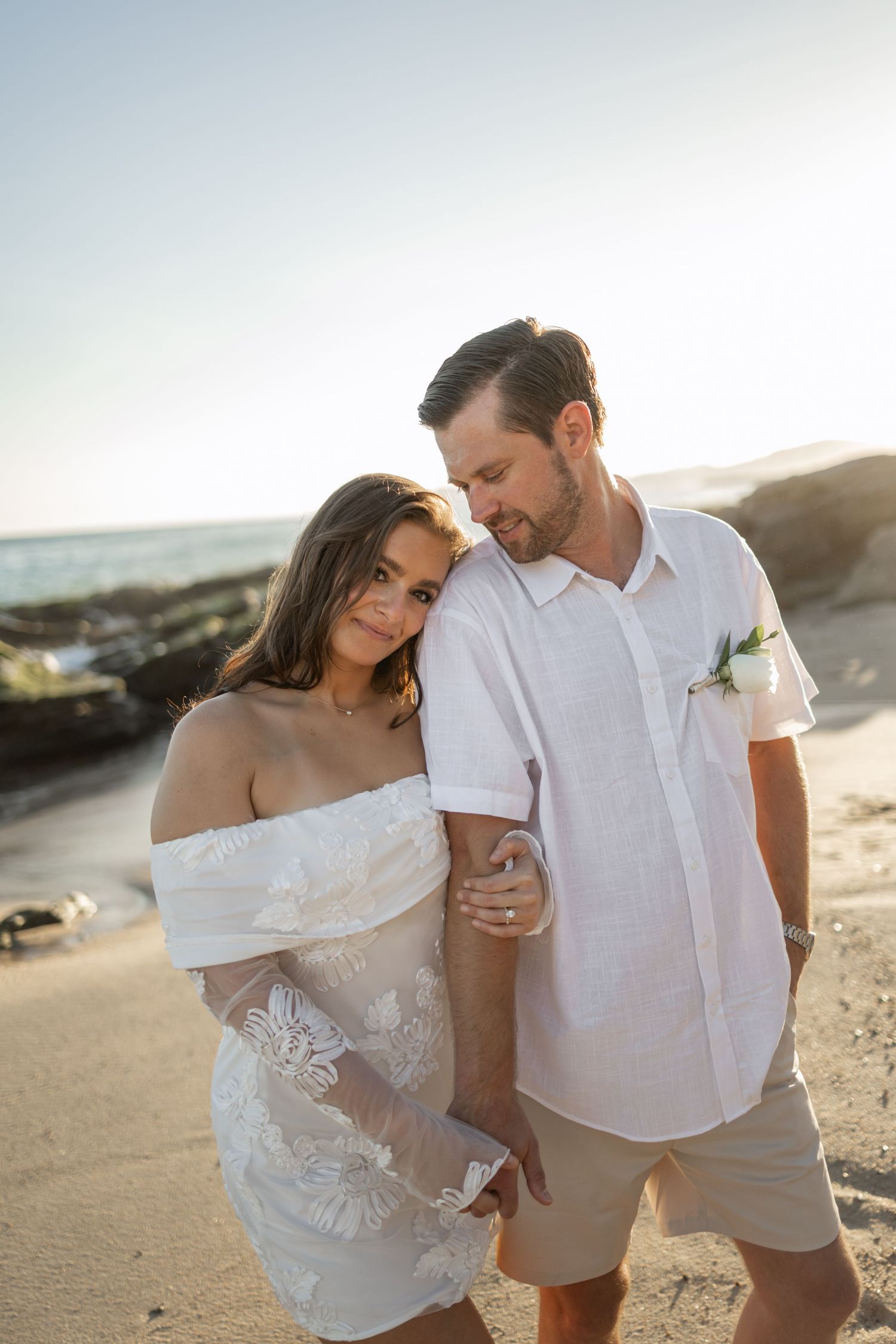 Romantic beach photoshoot with couple in white clothing during golden hour.
