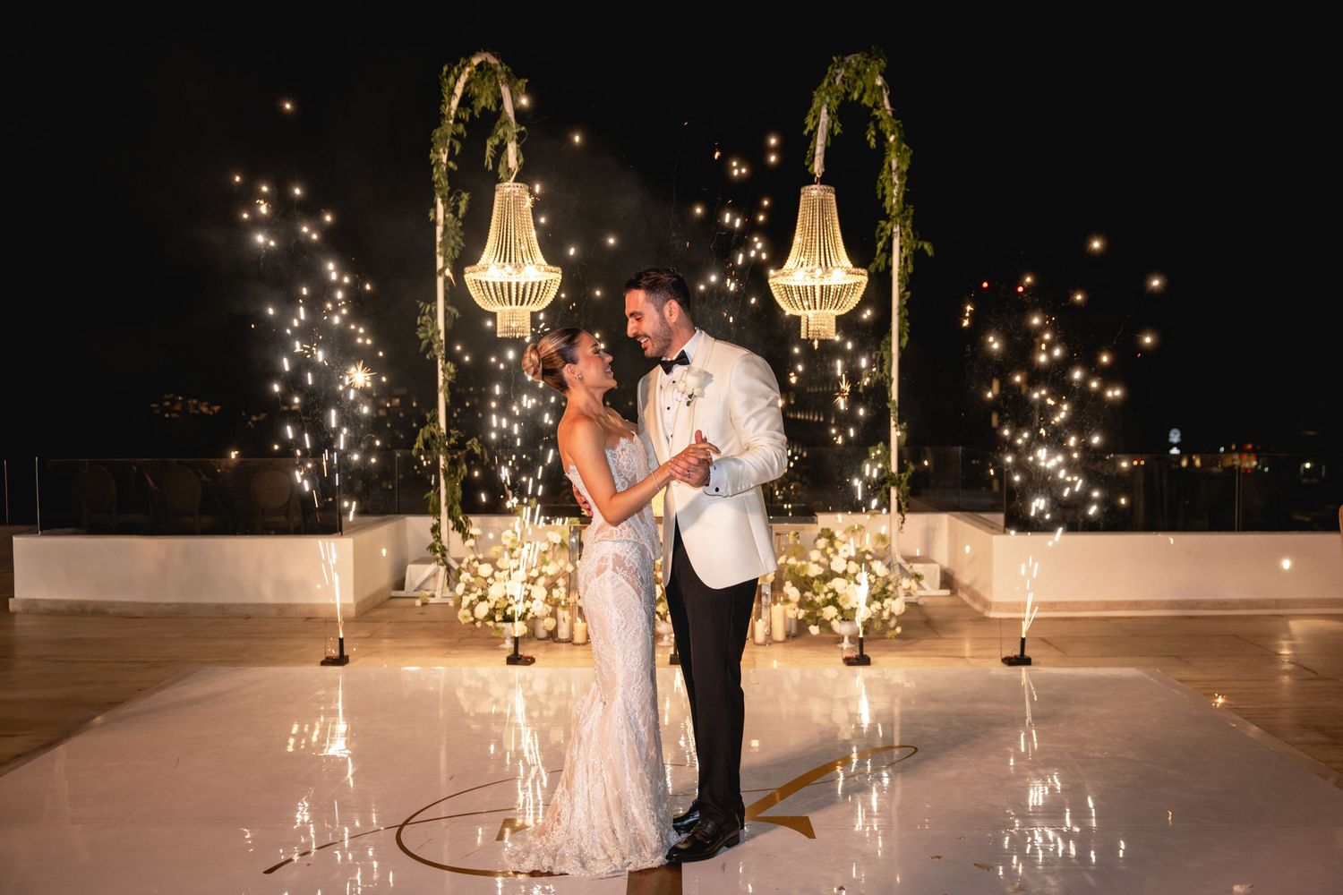 Elegant outdoor wedding reception setup with crystal chandeliers and twinkling lights at dusk.
