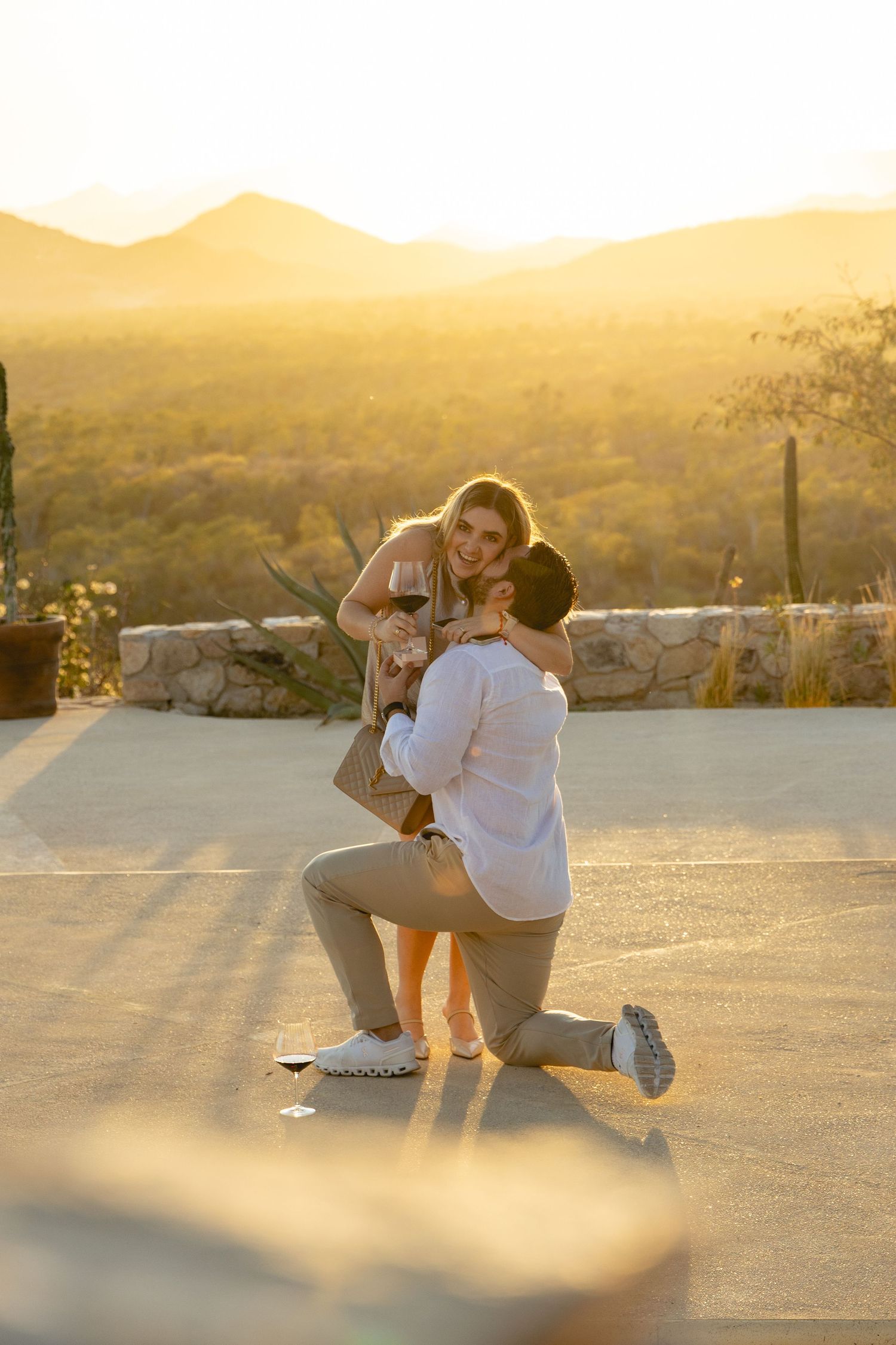 A couple sits together on a concrete surface at sunset in a desert landscape.