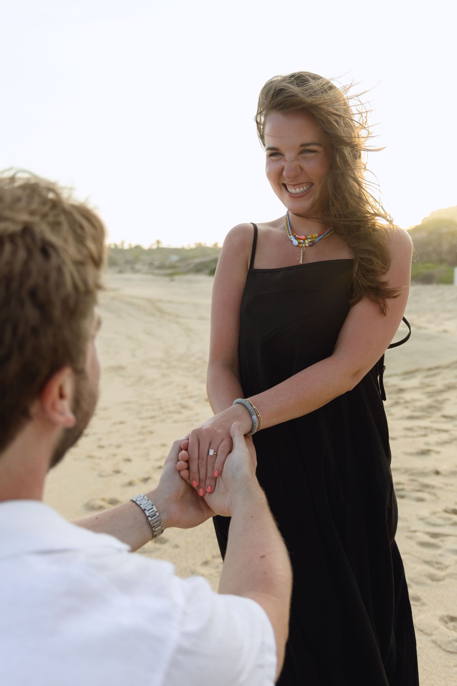A couple shares a romantic moment at sunset on a sandy beach as the wind blows through their hair.