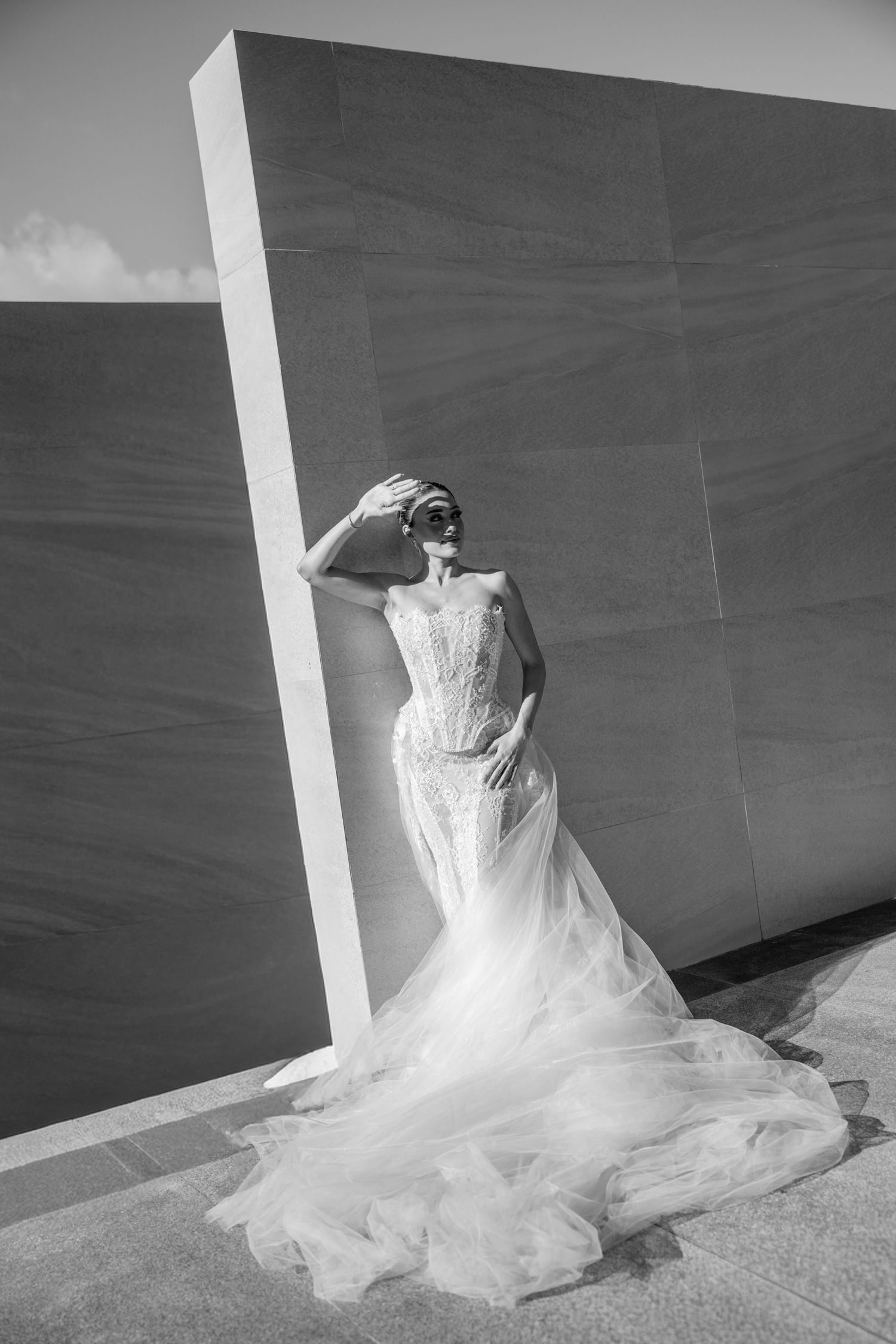 A wedding dress with flowing tulle fabric cascades down a white wall in an artistic black and white composition.