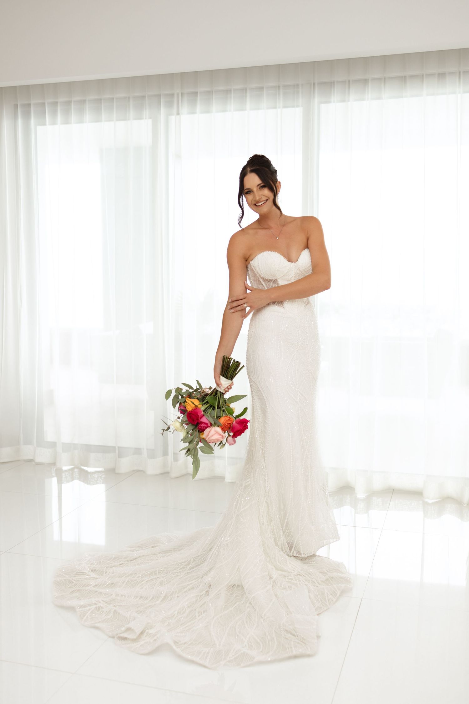 Elegant bridal portrait in a fitted lace wedding gown with trailing train and vibrant bouquet.