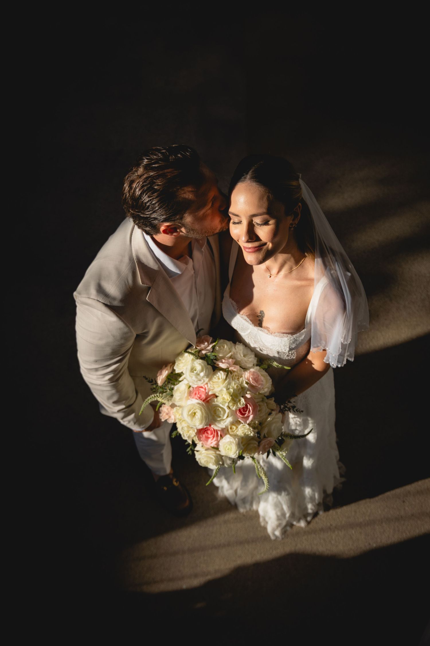 Intimate wedding moment captured from above with couple holding pink and white bouquet.