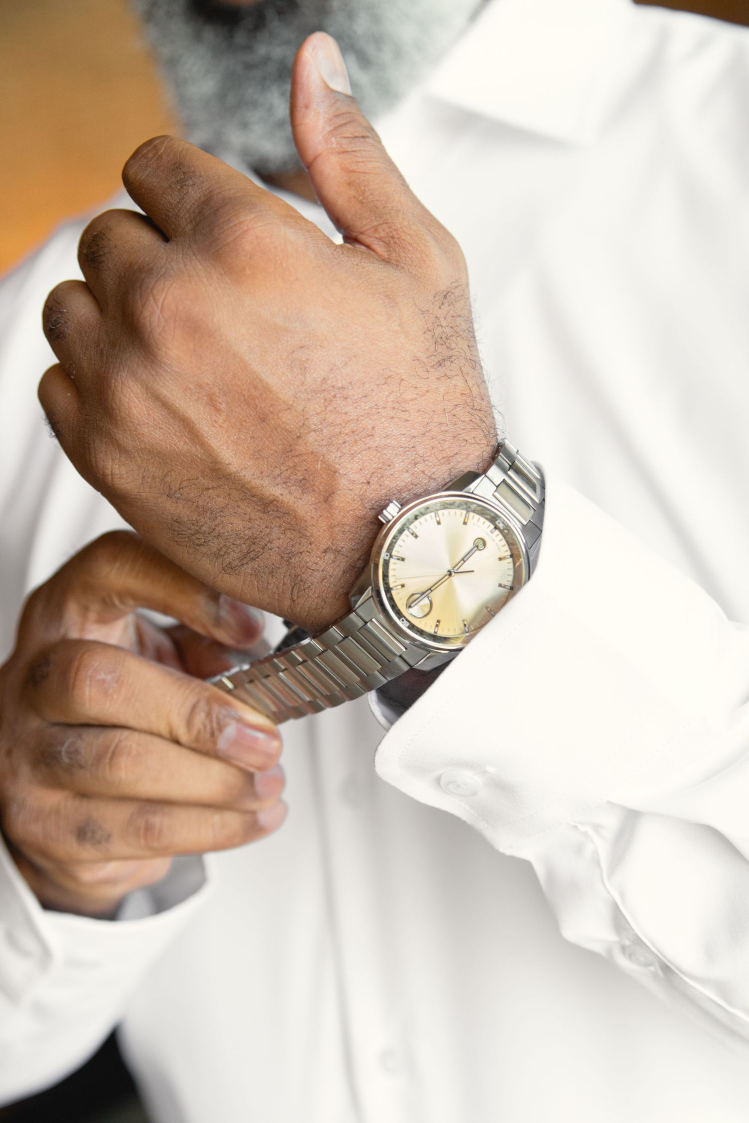 Hands adjusting silver watch and white dress shirt cuffs in sequence.