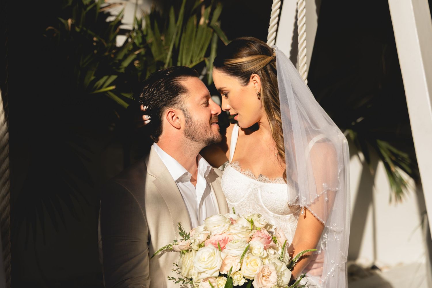 Intimate wedding moment shared between couple with tropical foliage in background.