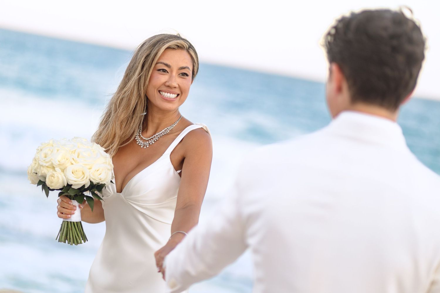 Beachside wedding couple in white attire sharing intimate moments by the ocean.