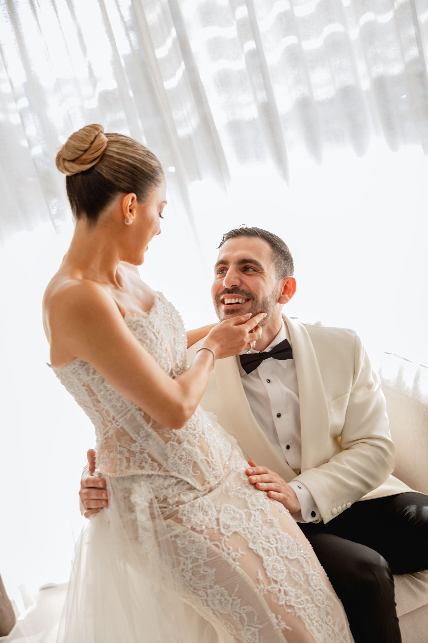 A tender moment between a couple on their wedding day, with the bride in lace and groom in white tuxedo.