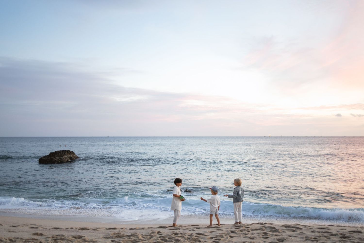 Scenic coastal sunset view with waves crashing on the beach and silhouettes of people enjoying the ocean at dusk.