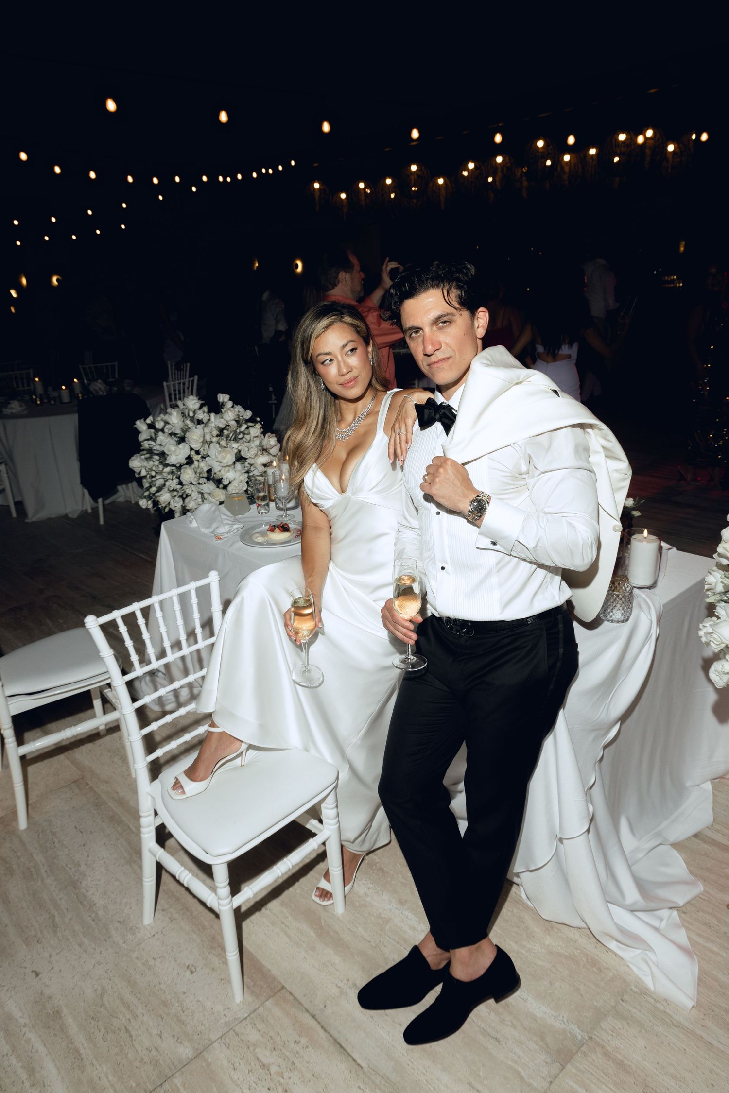 Newlyweds having fun with cake on the dance floor surrounded by white chairs and string lights.
