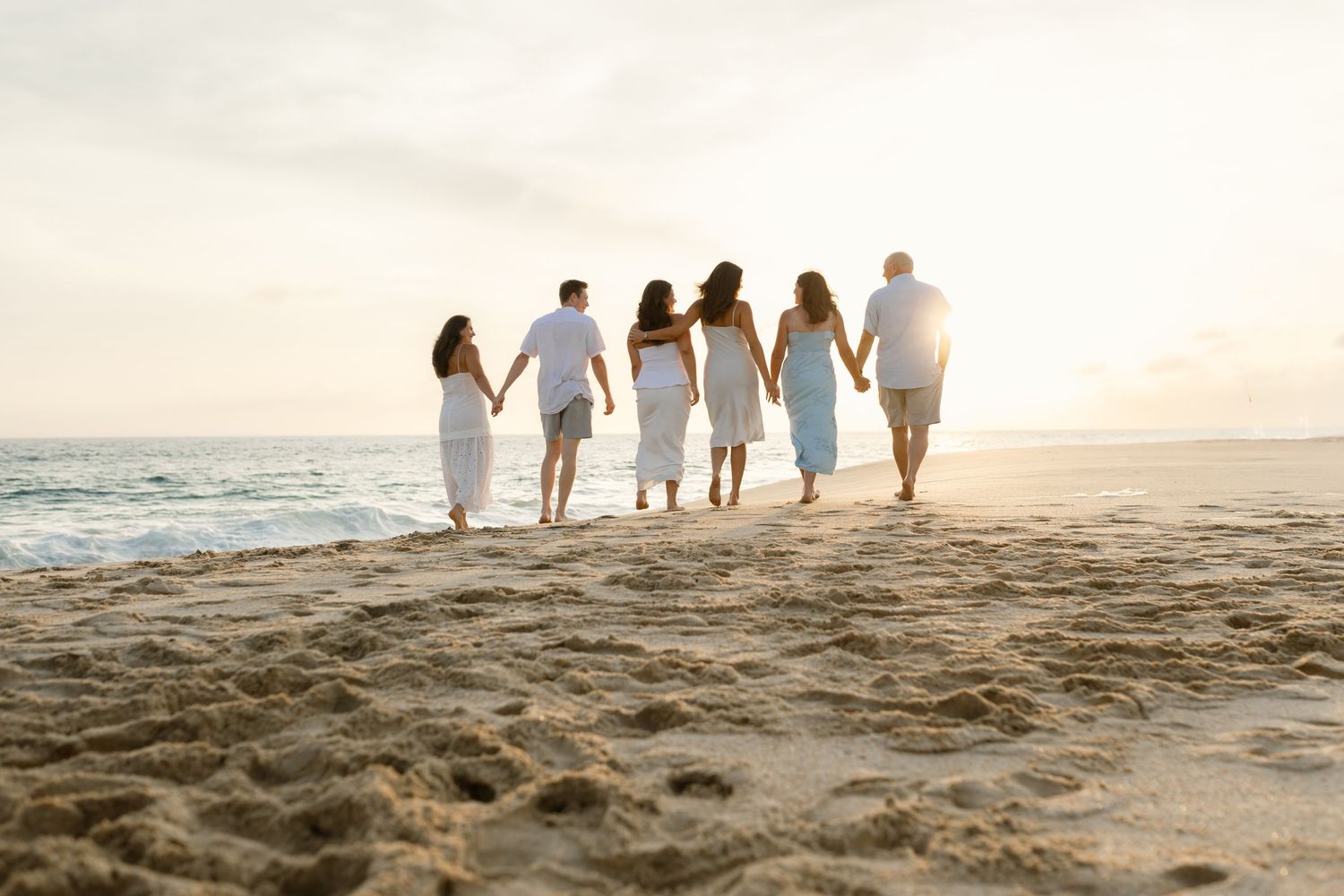 Group of people walking together along a sandy beach at sunset with golden light illuminating their silhouettes at Diamante, Los Cabos