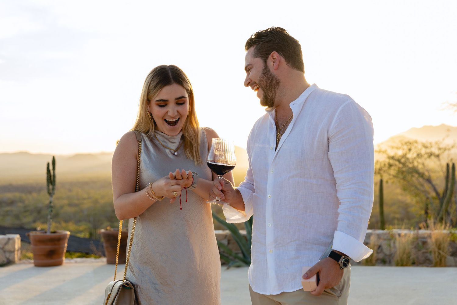 A couple enjoying drinks and conversation at sunset in a desert landscape with saguaro cacti in the background.