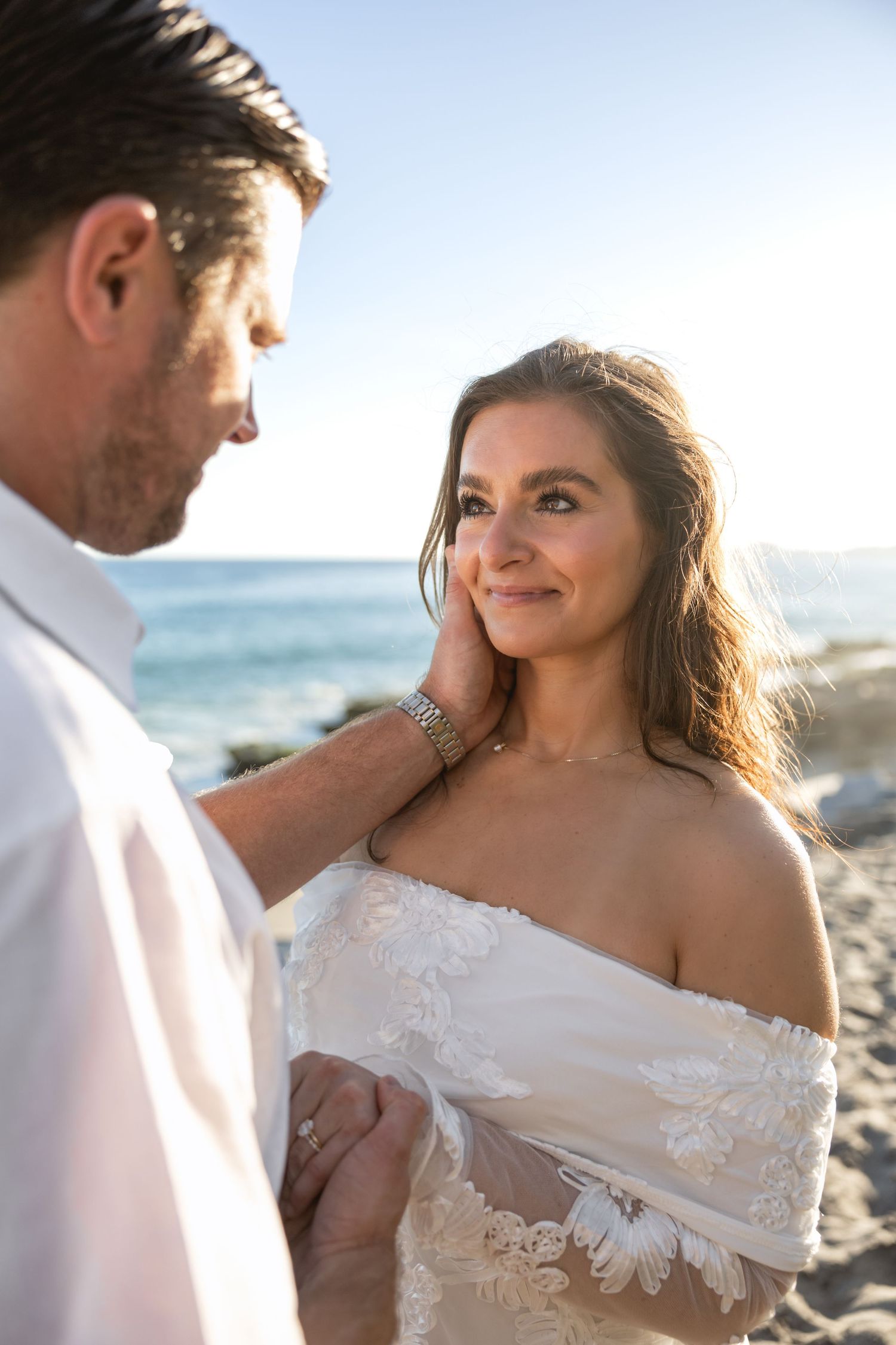 Romantic beachside photoshoot with couple in white attire against ocean backdrop.