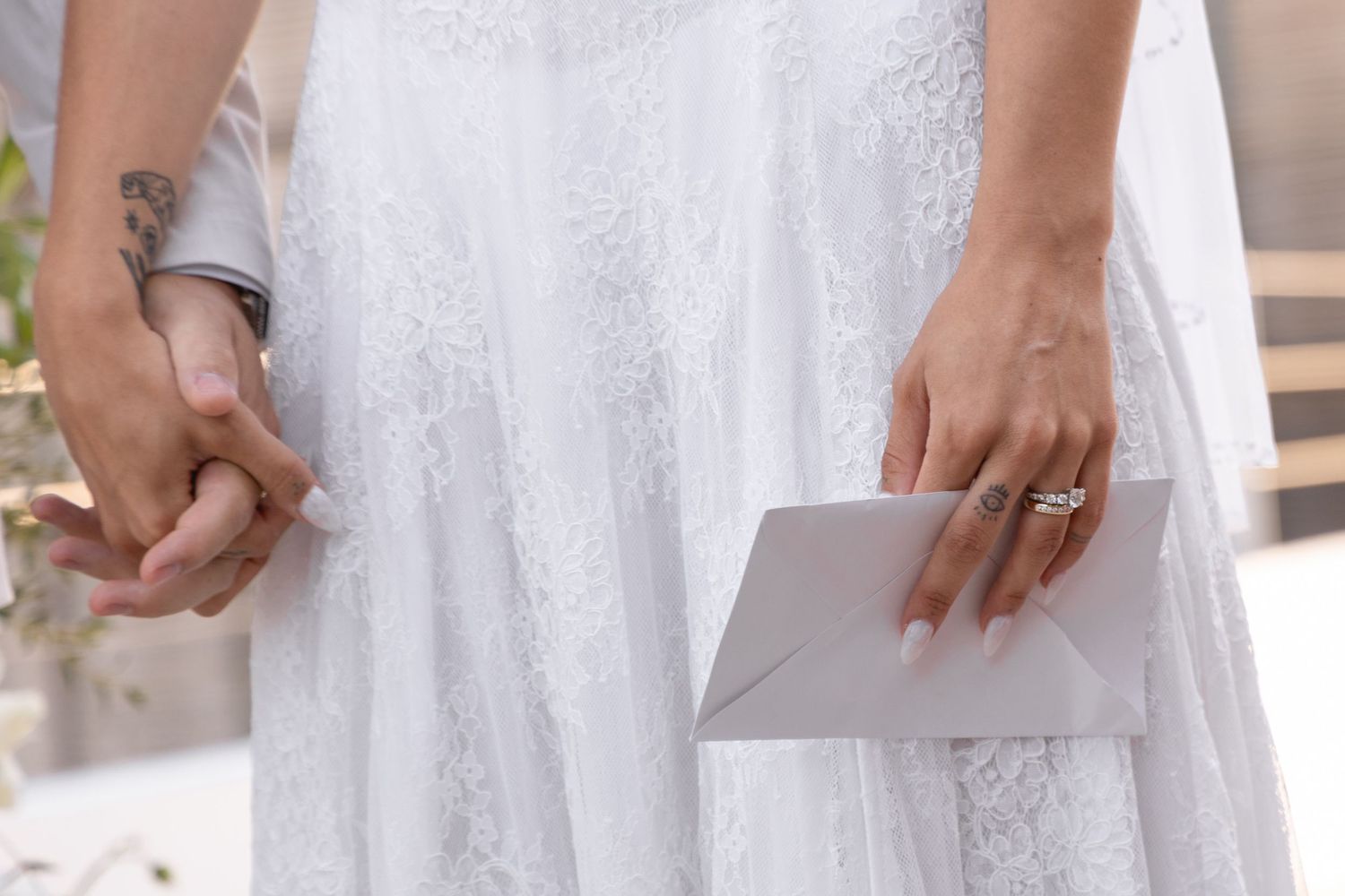 Close-up of hands holding a paper during a wedding ceremony with a lace dress visible.