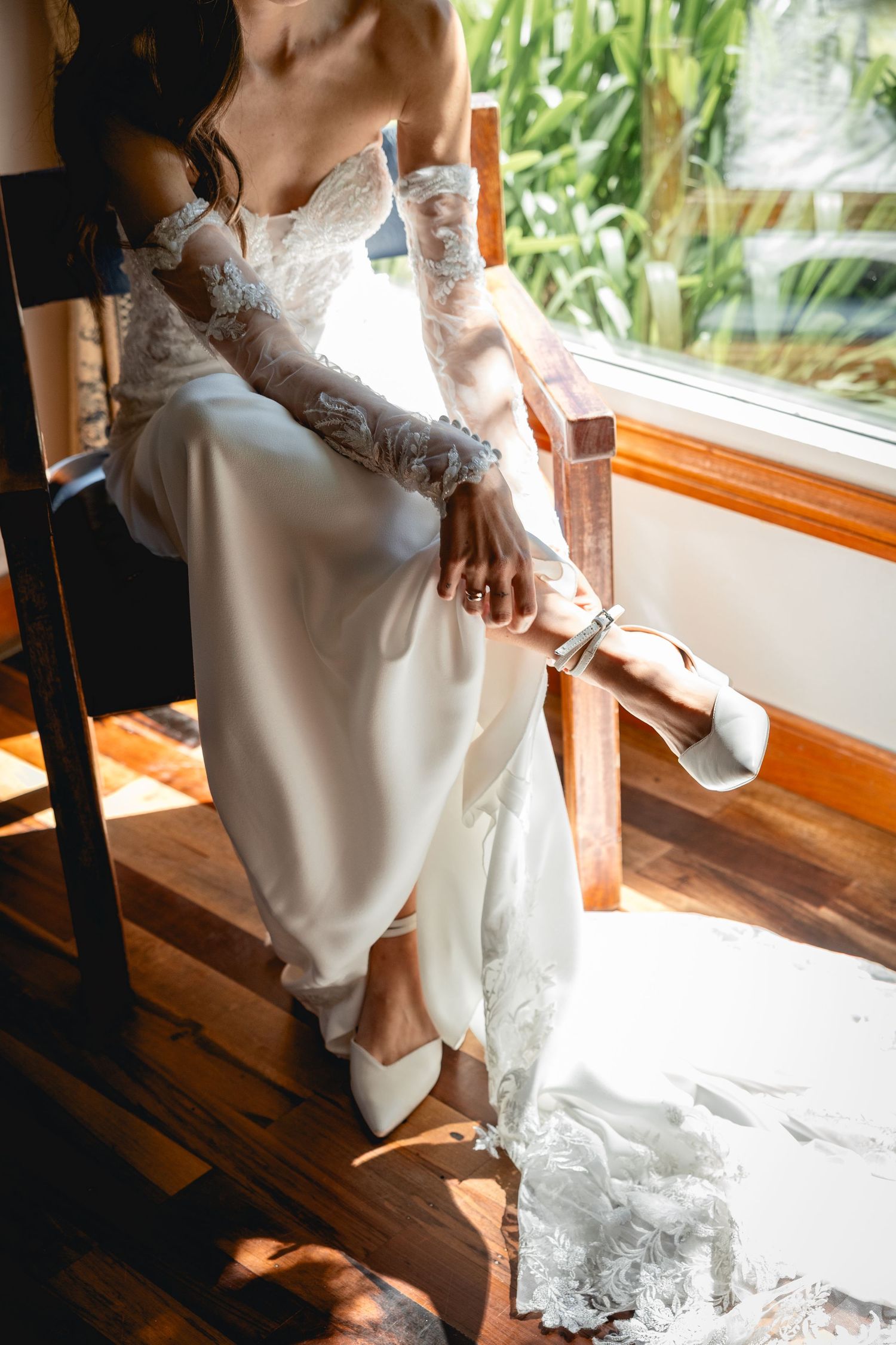 Elegant white lace wedding dress and shoes captured in sunlit window setting.