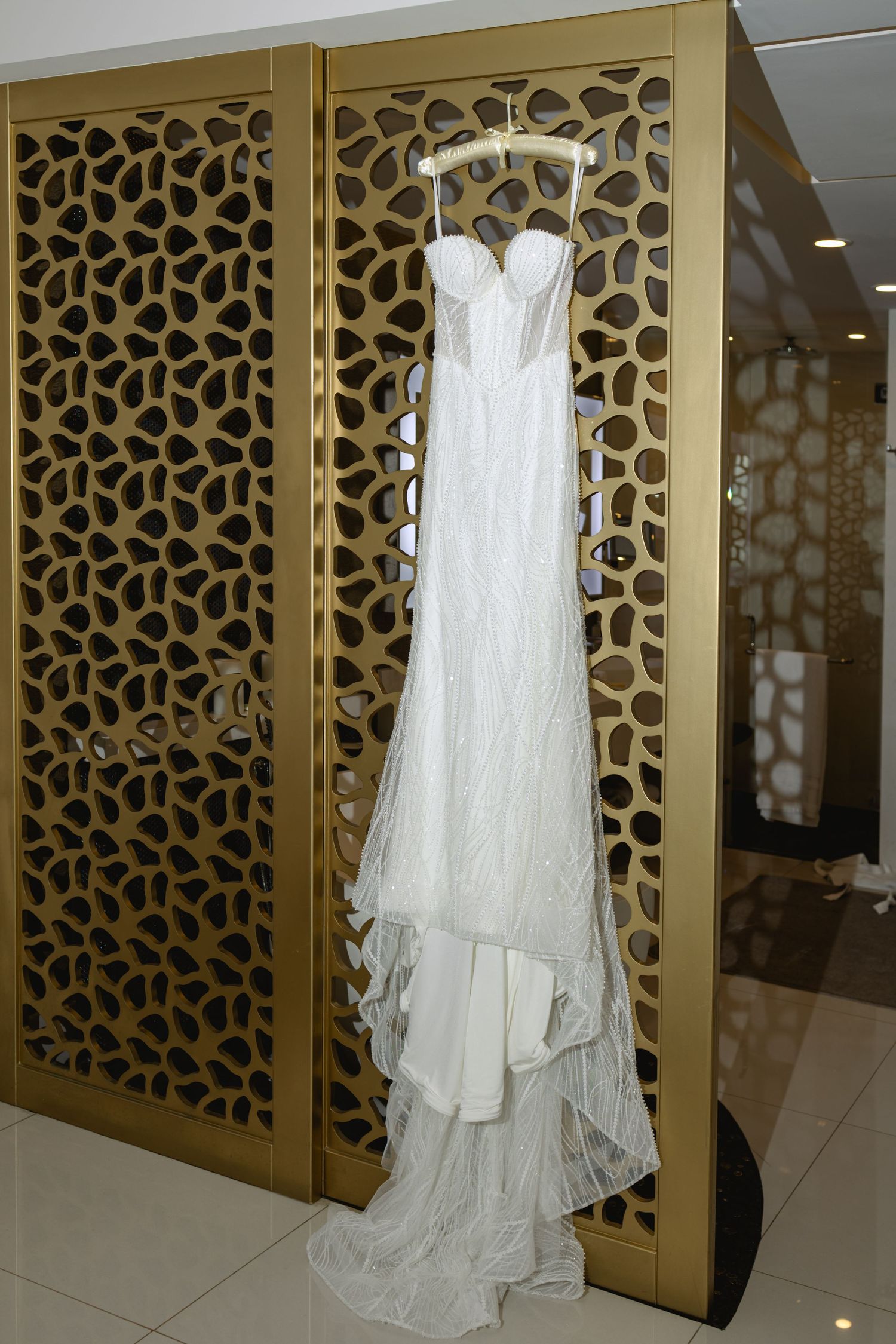 White wedding gown hanging against ornate gold geometric patterned wall.