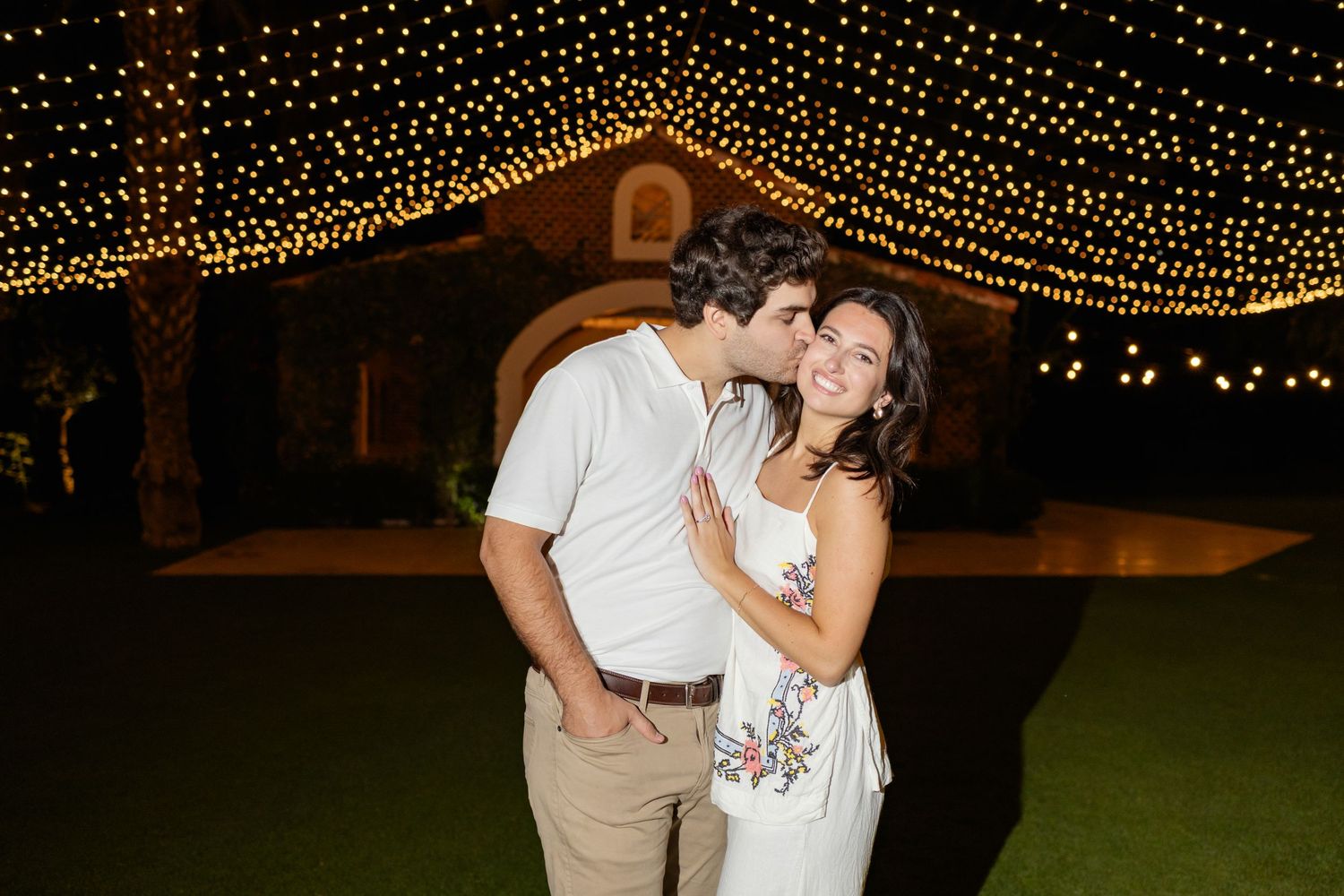 Romantic outdoor wedding reception under twinkling string lights with couples dancing on a warm evening.