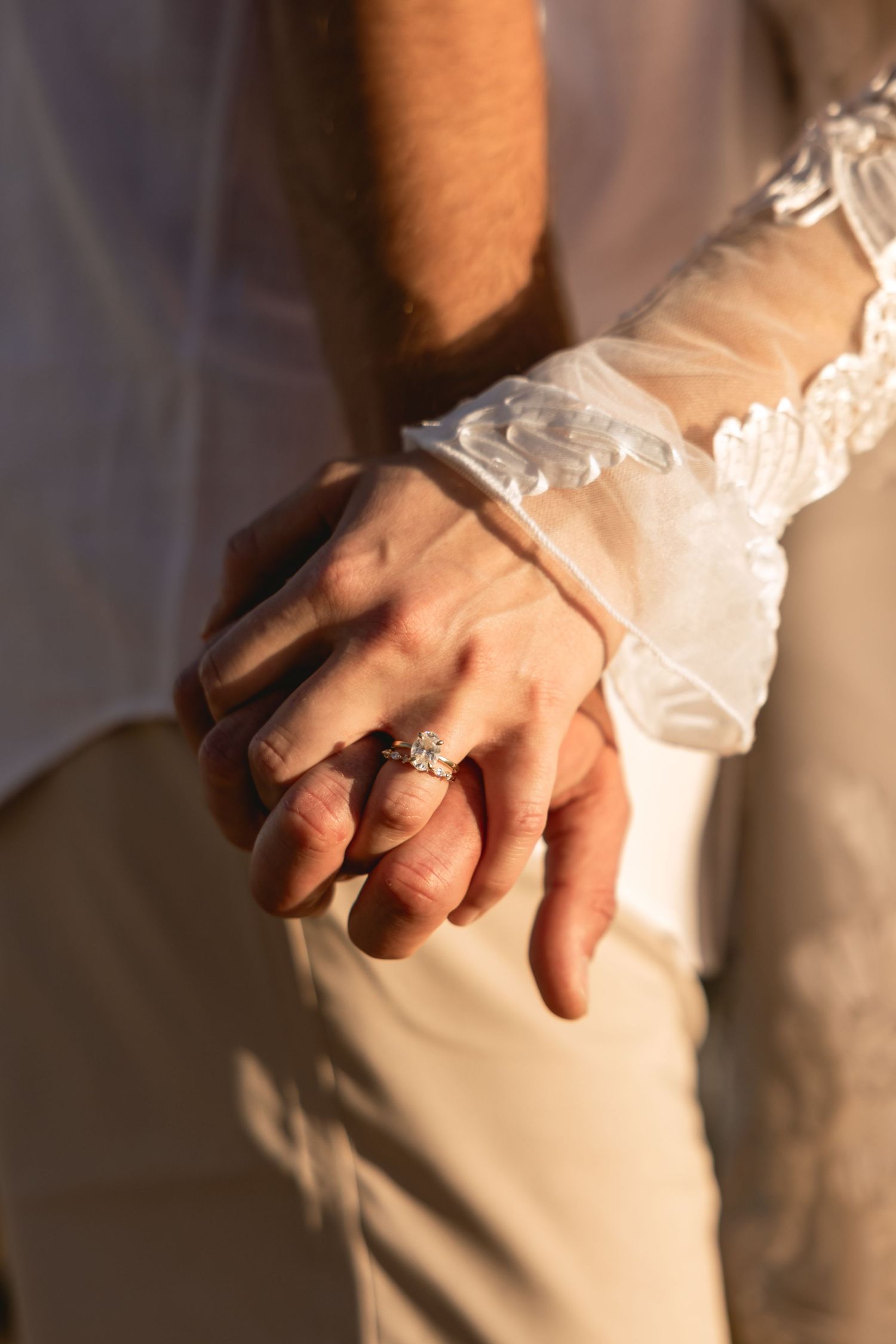 Close-up detail shot of hands with engagement ring in warm sunlight.