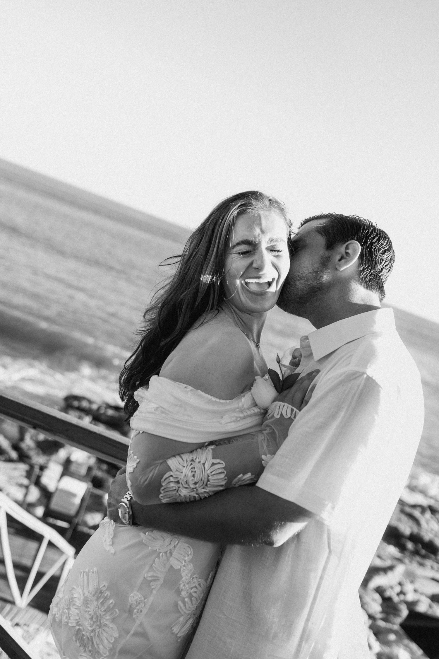 A black and white photo captures an intimate moment between a couple on the beach.
