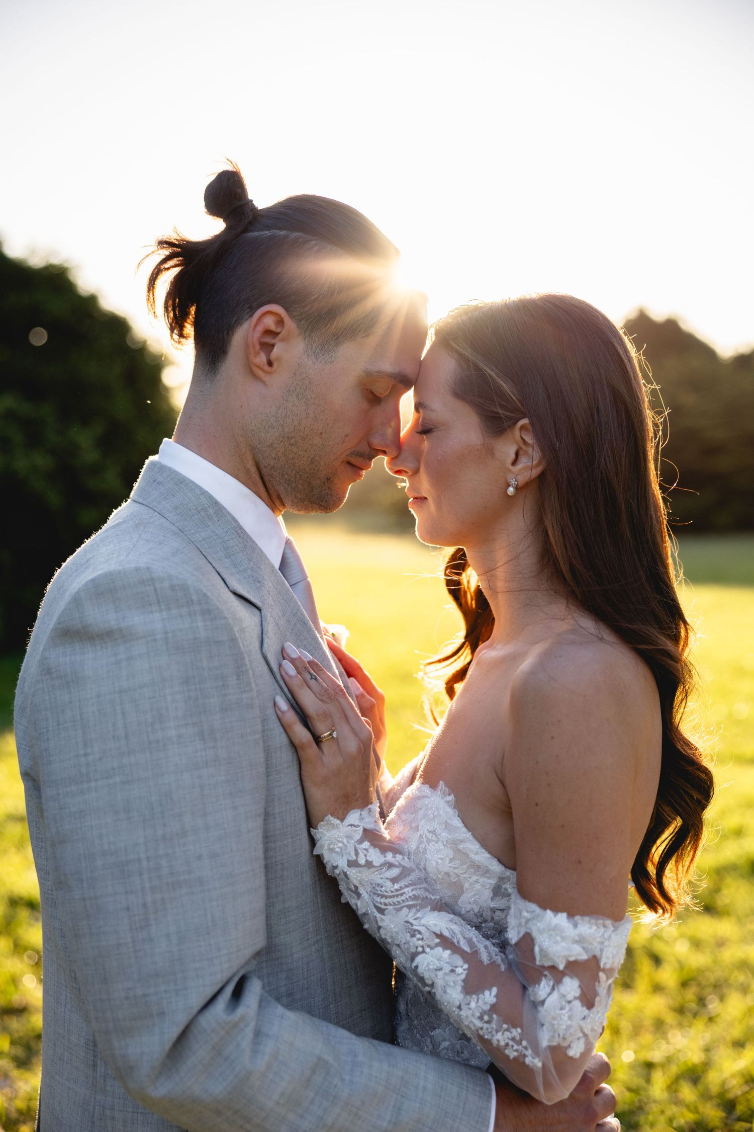 Romantic wedding couple embraces in a golden sunlit field during sunset.
