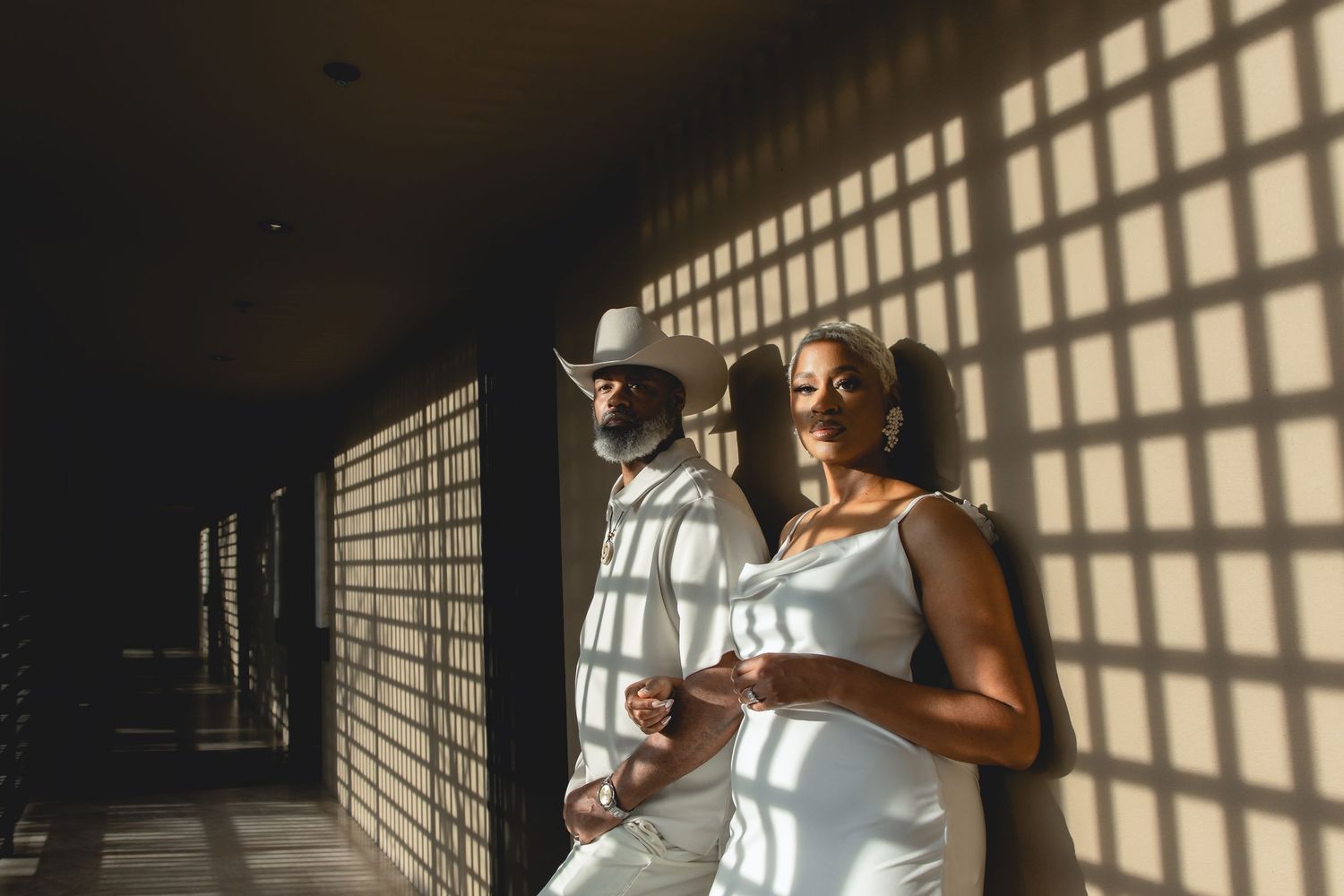Dramatic window light creates geometric shadows on wall behind couple in white.