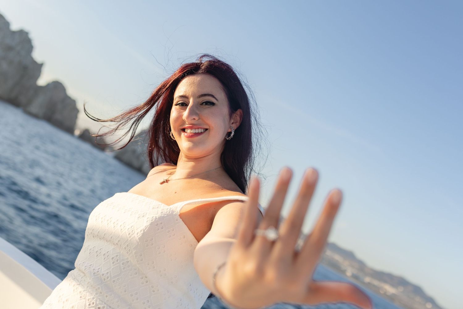 Someone in a white top waves at the camera while enjoying a sunny day near the ocean.