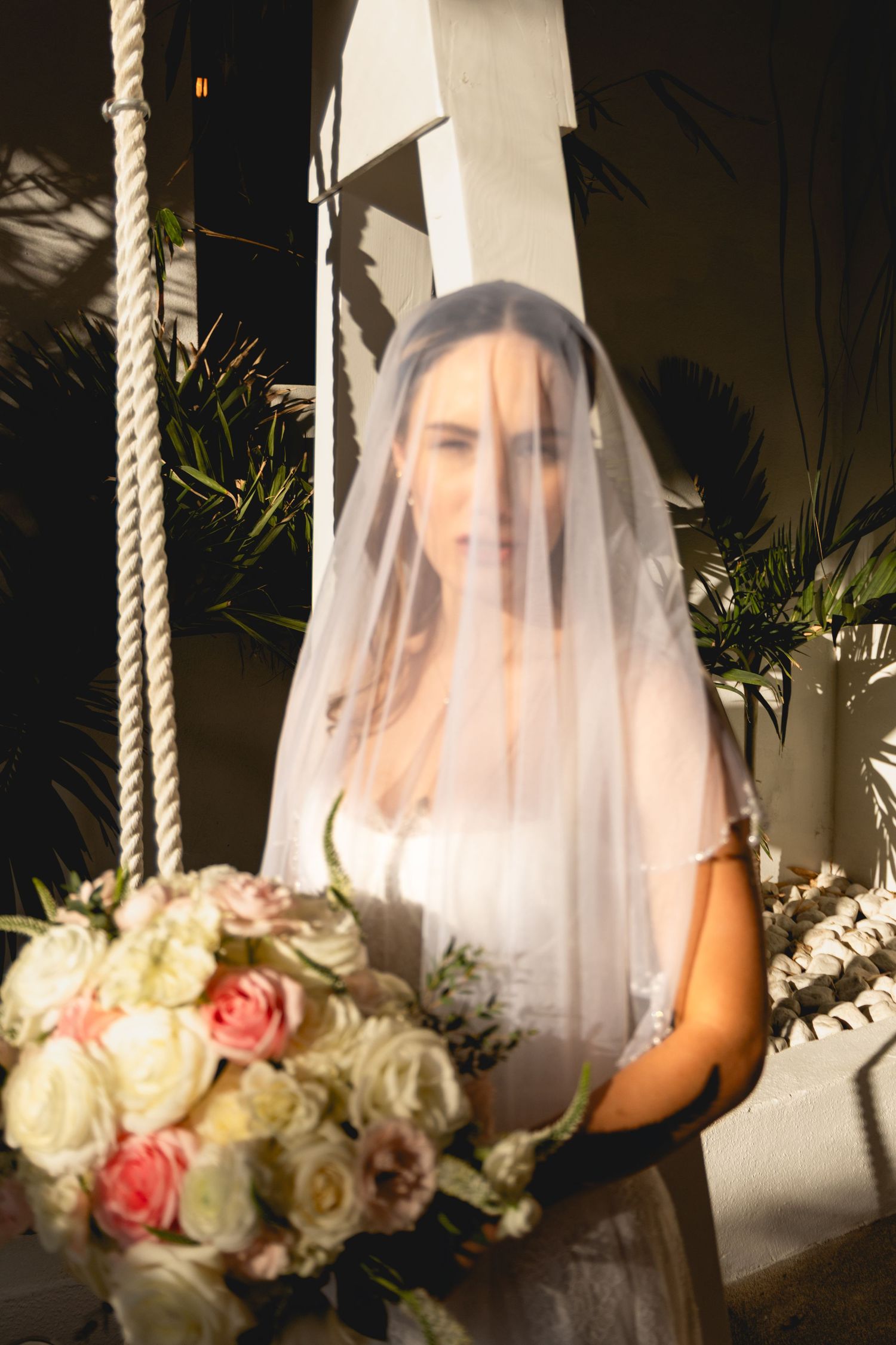 Bride in white veil holding elegant bouquet of roses in dramatic lighting.