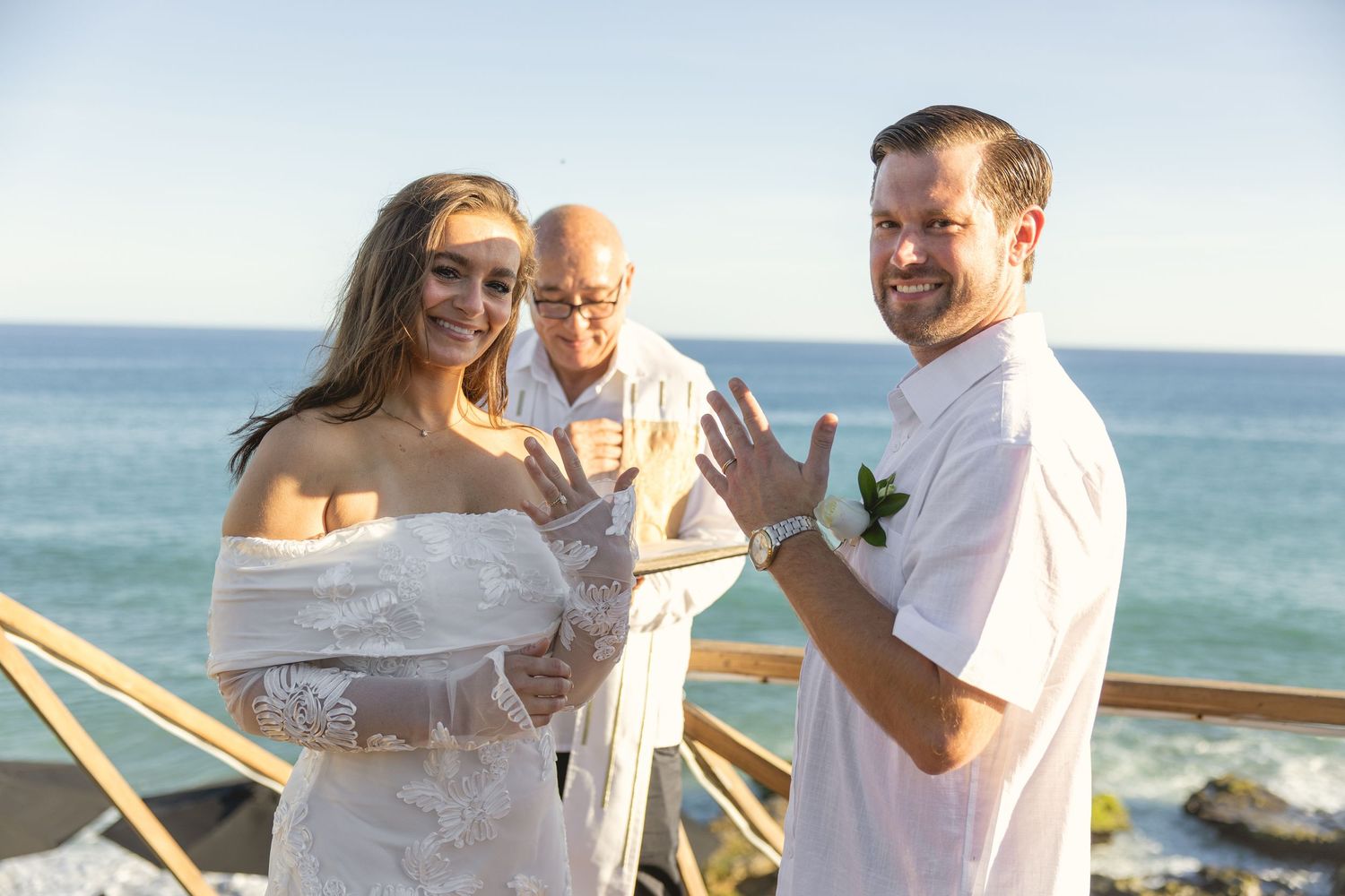 Beachside wedding ceremony with ocean backdrop and wooden railing.