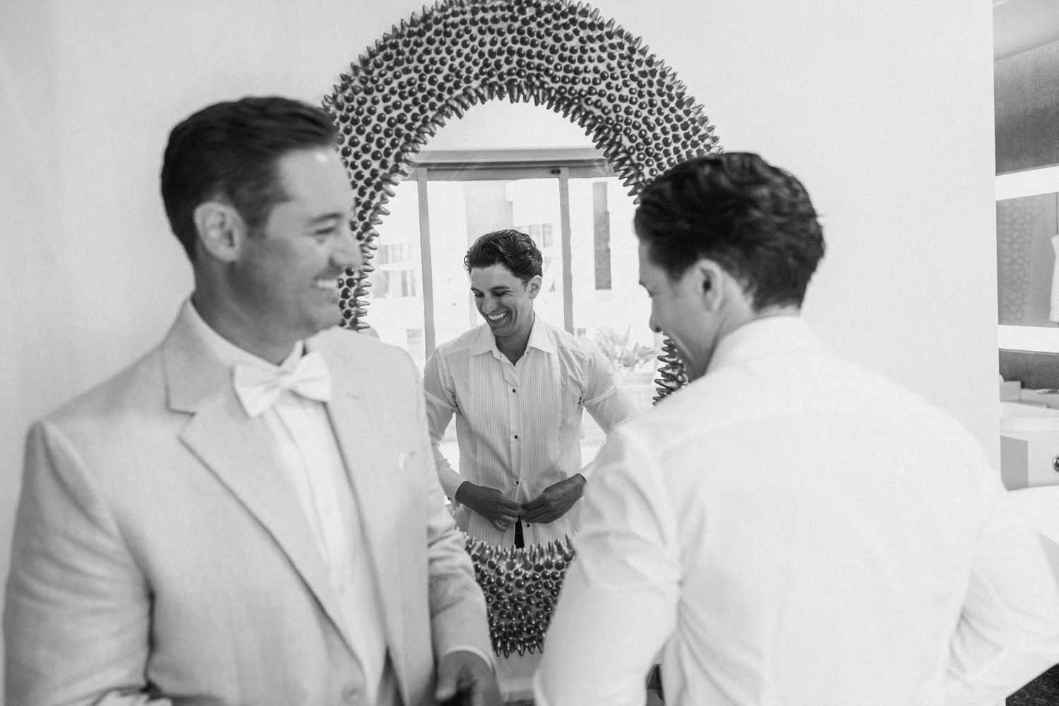 Groomsmen in light suits sharing laughs before wedding ceremony.