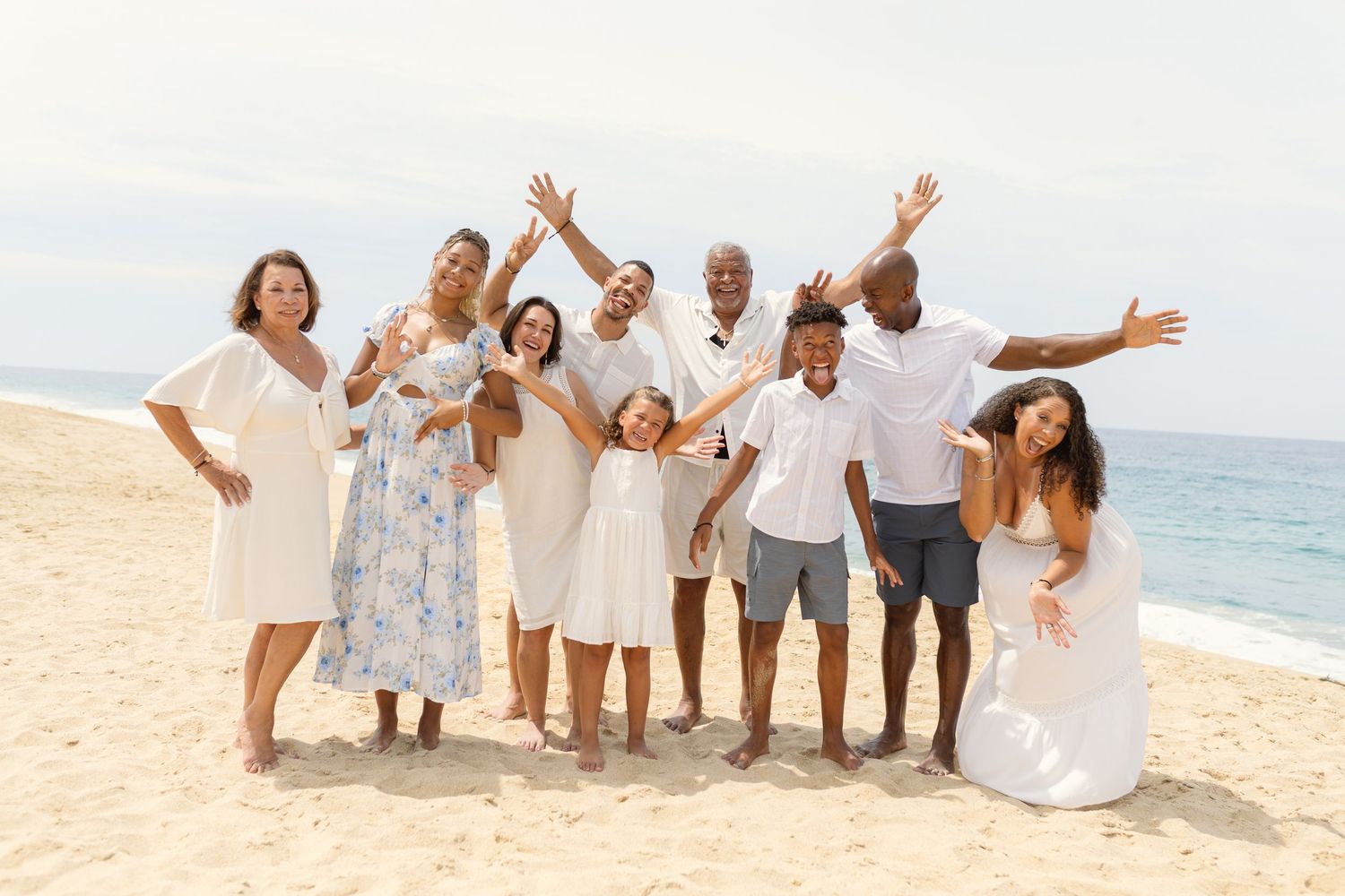 Group of people in coordinated white and blue outfits posing joyfully together on a sunny beach at diamante Cabo San Lucas