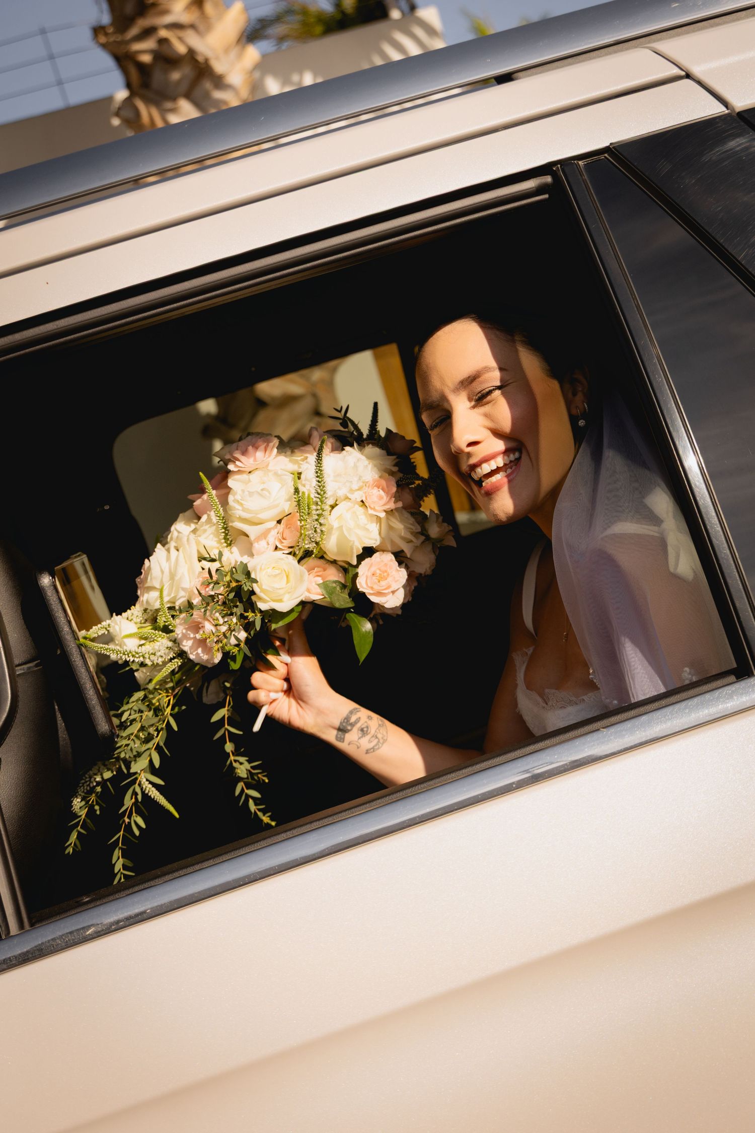 Wedding party looking through limousine window with white roses and greenery.