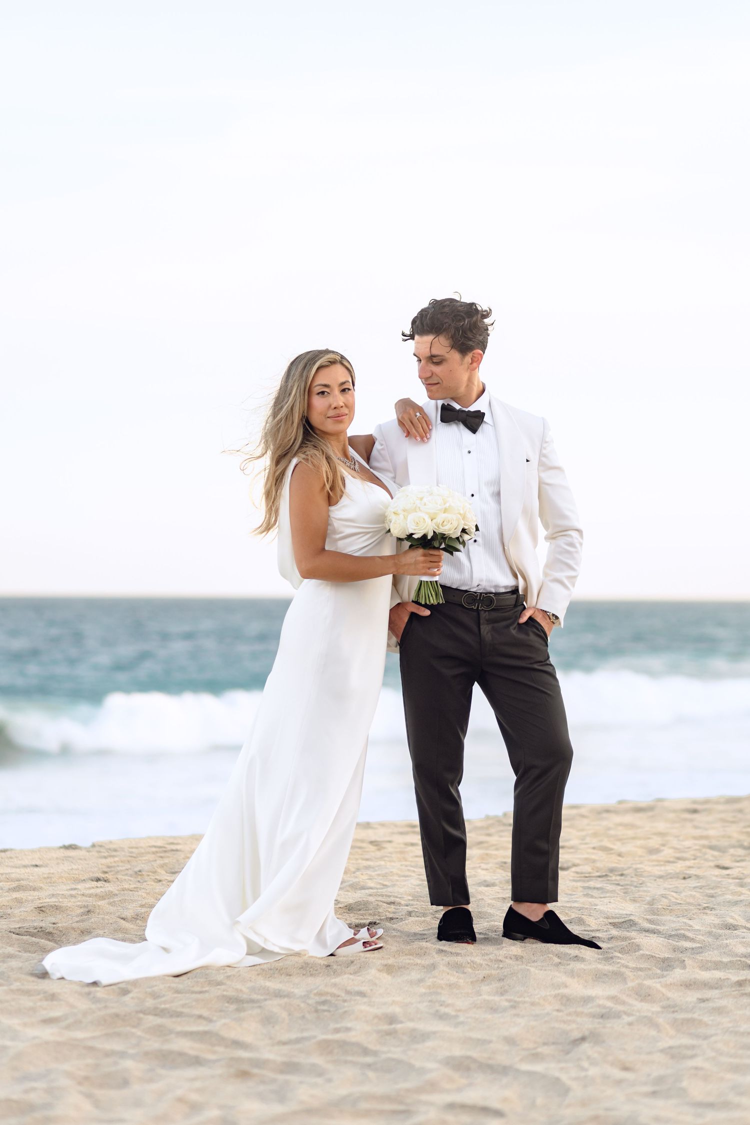 Elegant beach wedding portrait with couple in white and black formal wear.