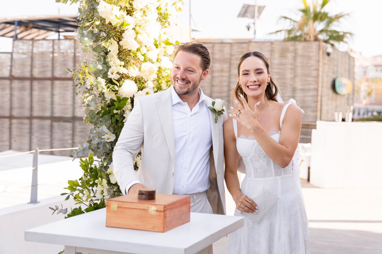 A couple stands at a white table with a wooden box during their wedding ceremony.