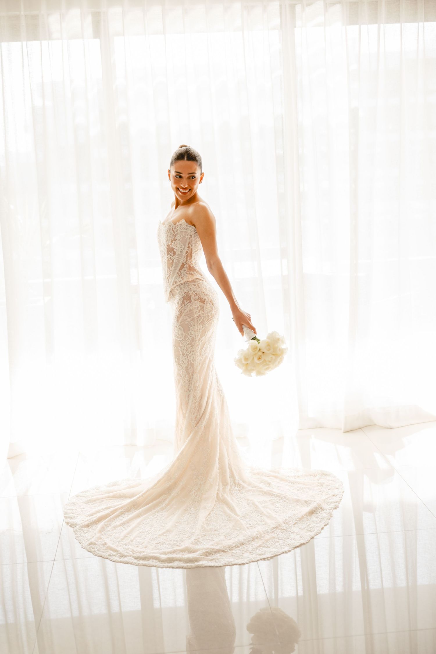 Elegant bridal portraits showing flowing train of lace wedding gown in bright setting.