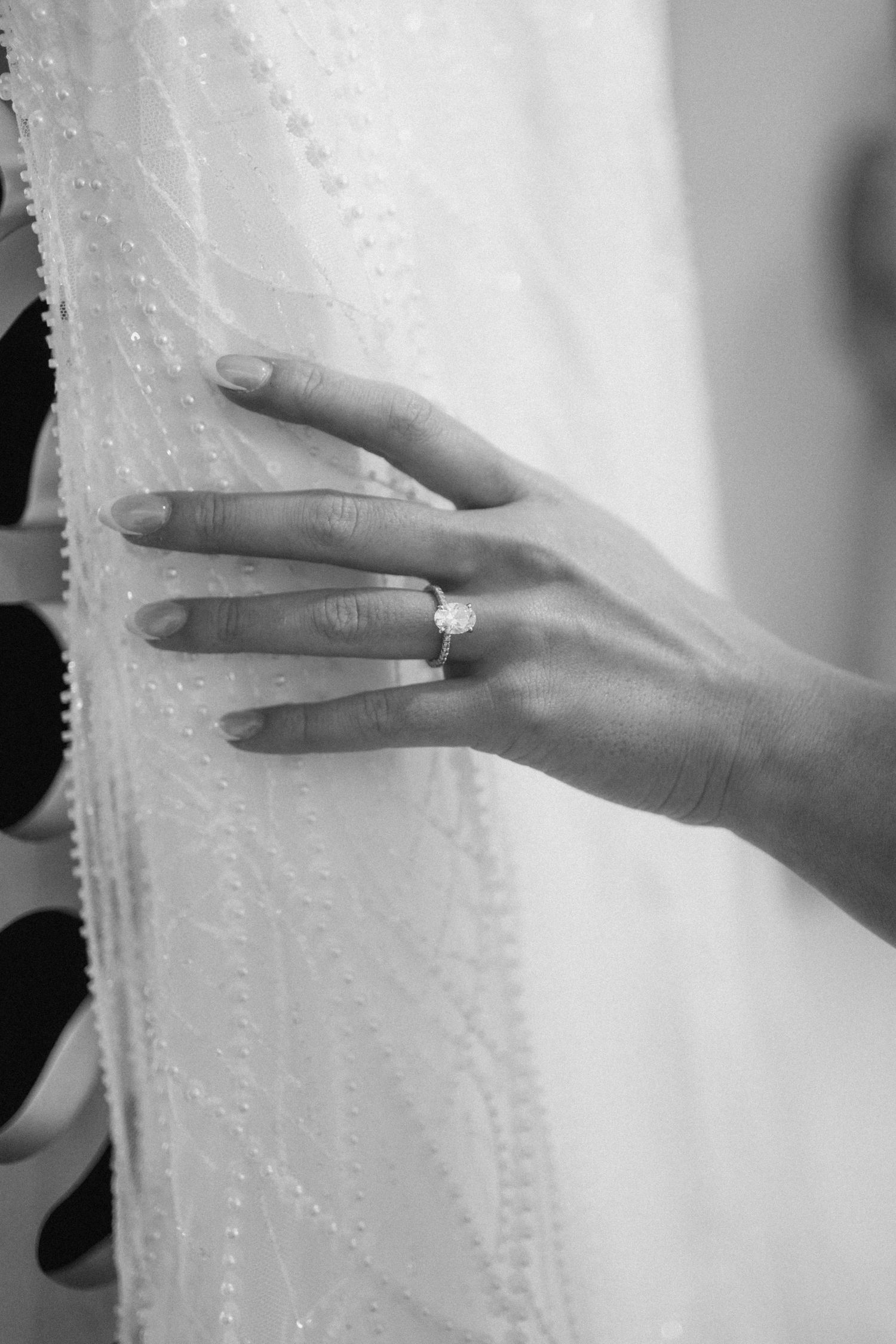 Close-up of delicate beaded wedding dress details with hand displaying ring.