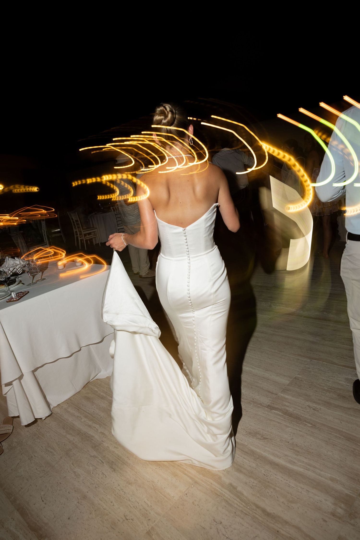 Bride and groom share first dance at night wedding reception with glowing light trails in background.