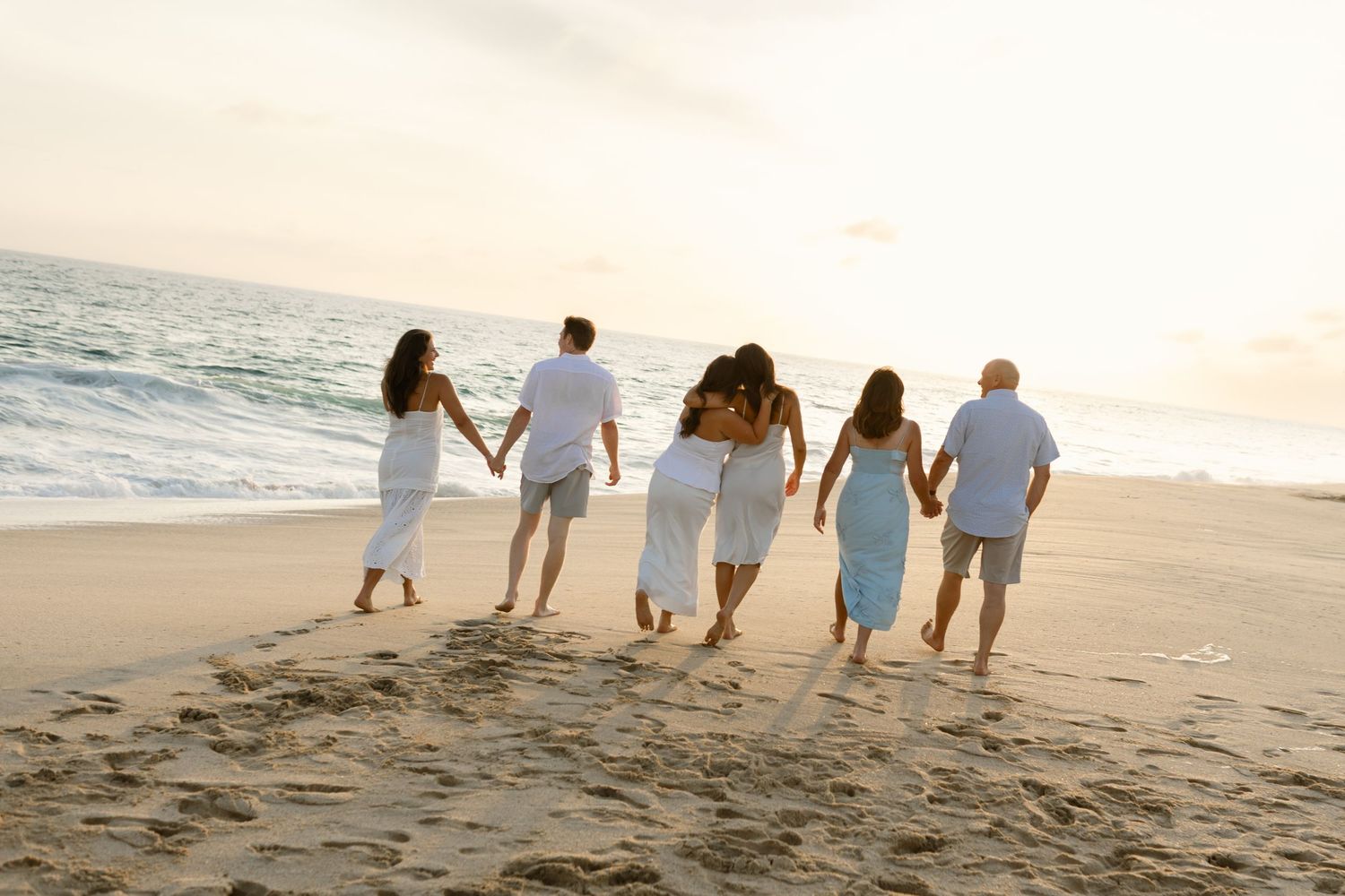 Family walking together along a scenic beach at sunset holding hands.