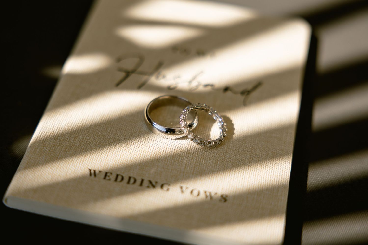 Wedding rings casting dramatic shadows on white wedding vows paper.